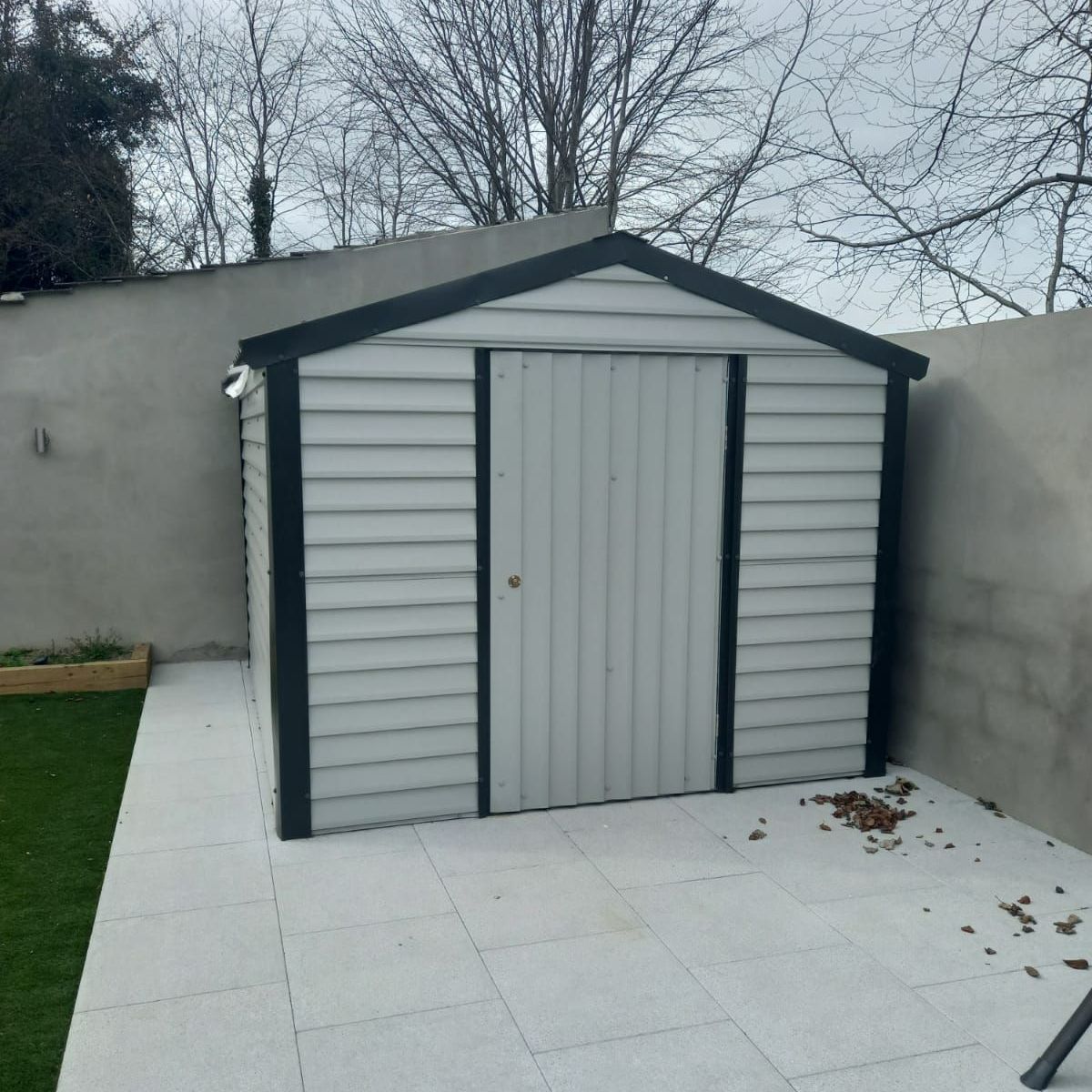 A white shed with a black trim sits in a backyard