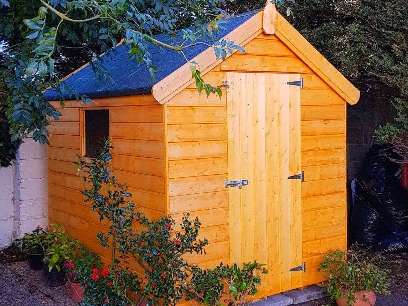 A wooden shed with a blue roof is surrounded by potted plants.
