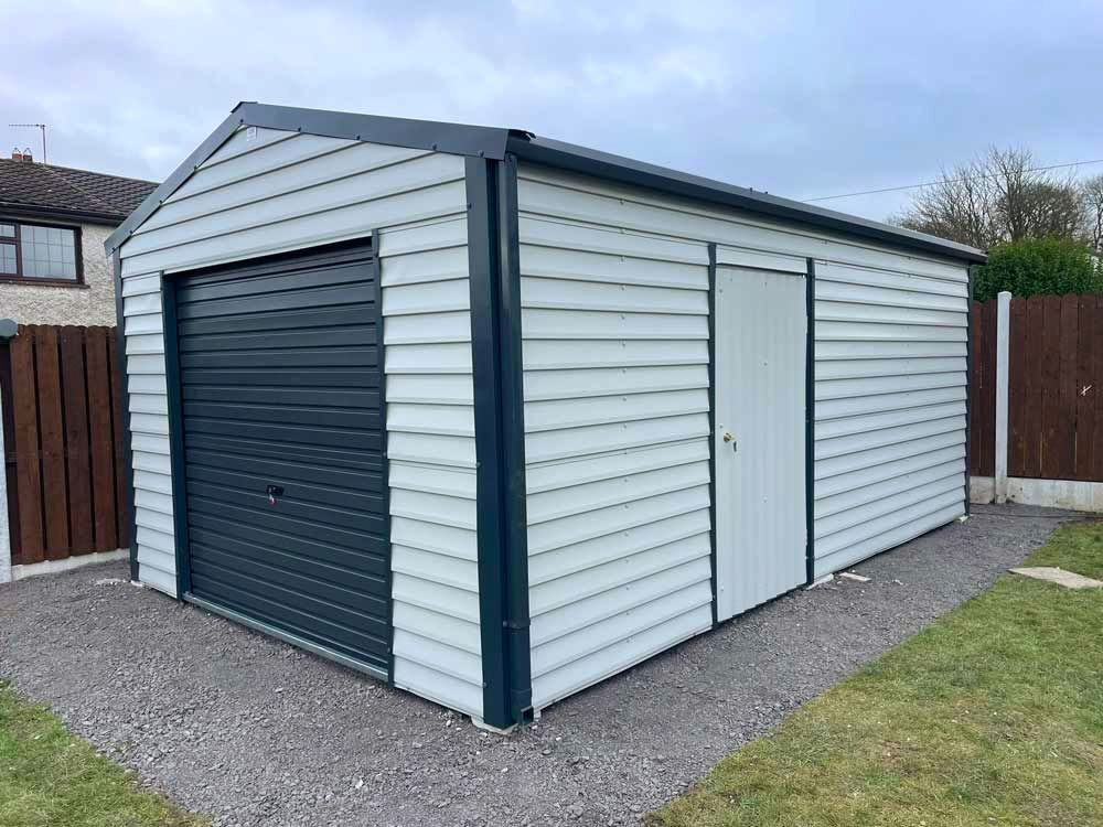 A white garage with a black garage door is in the backyard of a house.