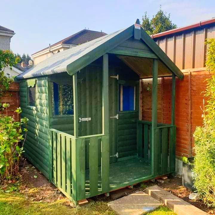 A green wooden playhouse is sitting in the backyard next to a wooden fence.