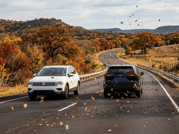 Volkswagen Tiguan and SUV driving along a winding Texas road surrounded by colorful fall foliage
