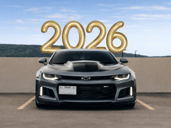 Gray sports car in a parking lot with large gold “2026” numbers above it