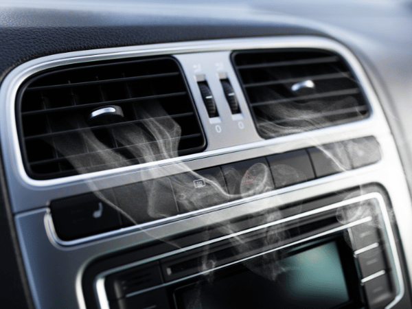 Car dashboard air vents releasing smoke to represent musty or unusual AC odors
