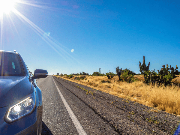 Blue SUV parked along a rural desert highway with cacti, dry grass, and bright Texas sunshine overhead.