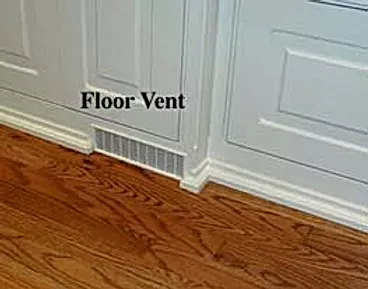 A floor vent is built into a wall next to a hardwood floor.