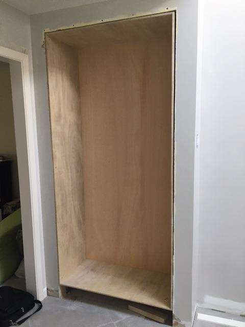 A wooden shelf is being built into a wall in a room.