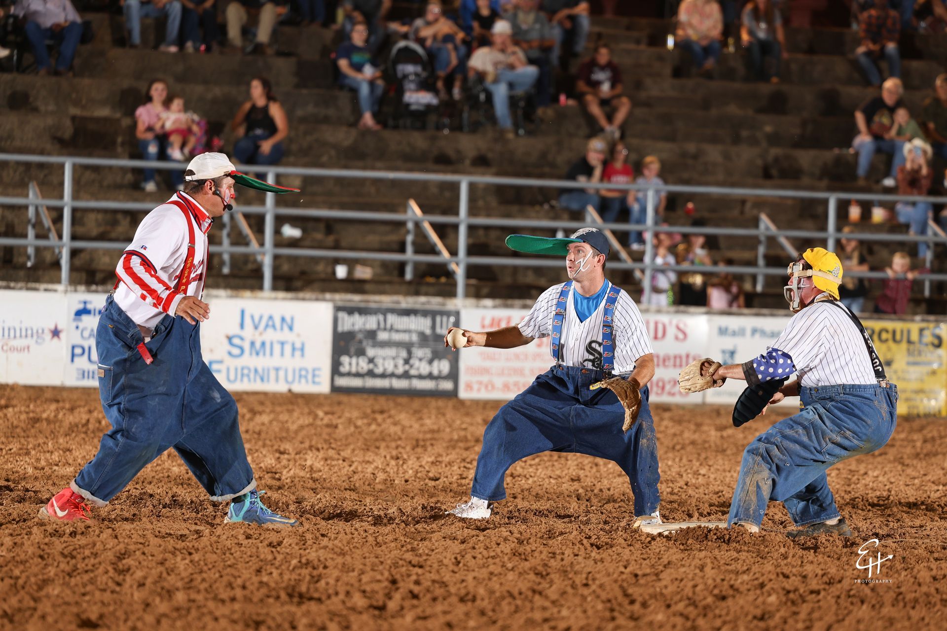 Three people in a dirt-field game, crouched low and facing each other as a crowd watches in the stands.