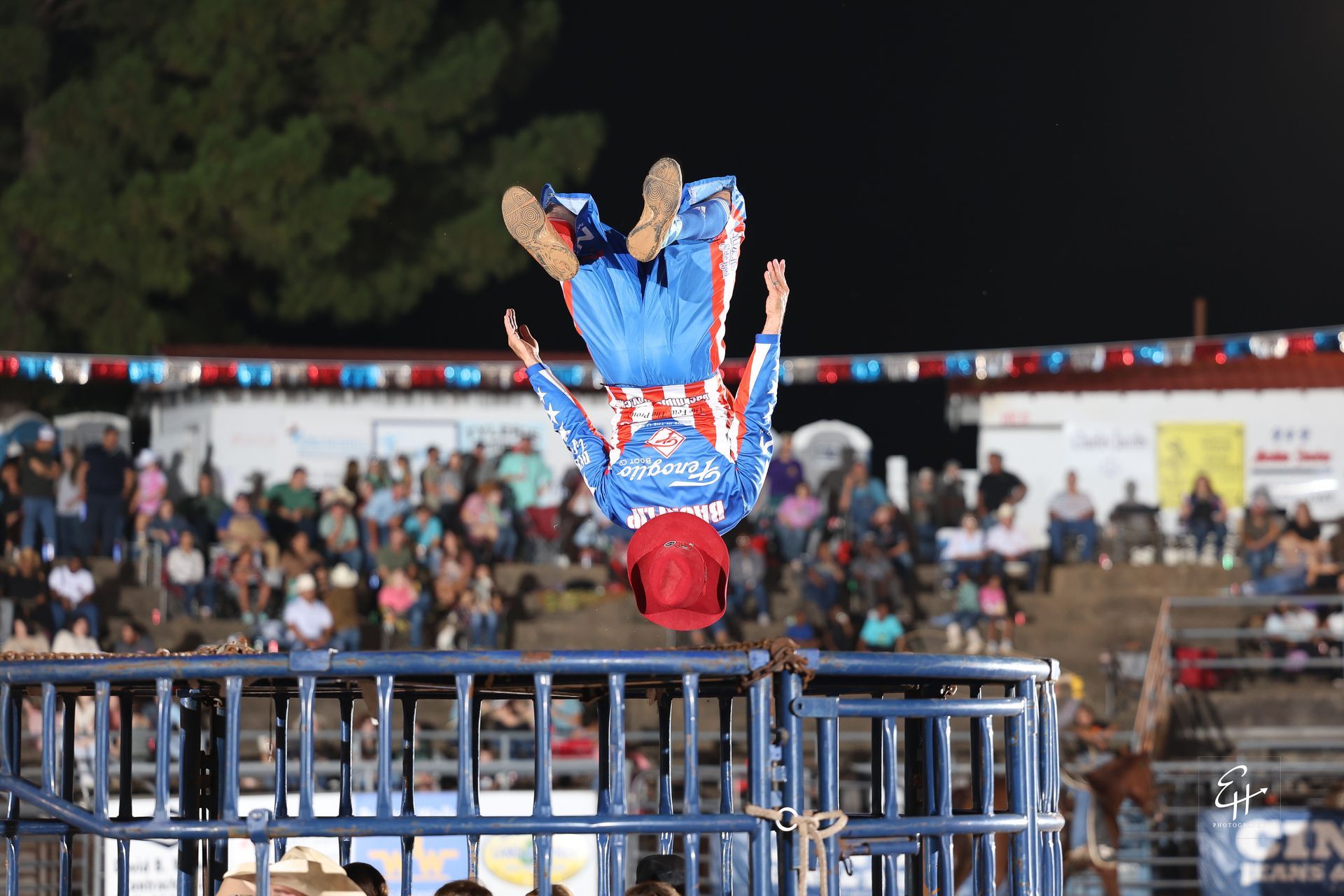 Acrobat in red and blue performs an upside-down handstand on a metal barrier before a crowd at night