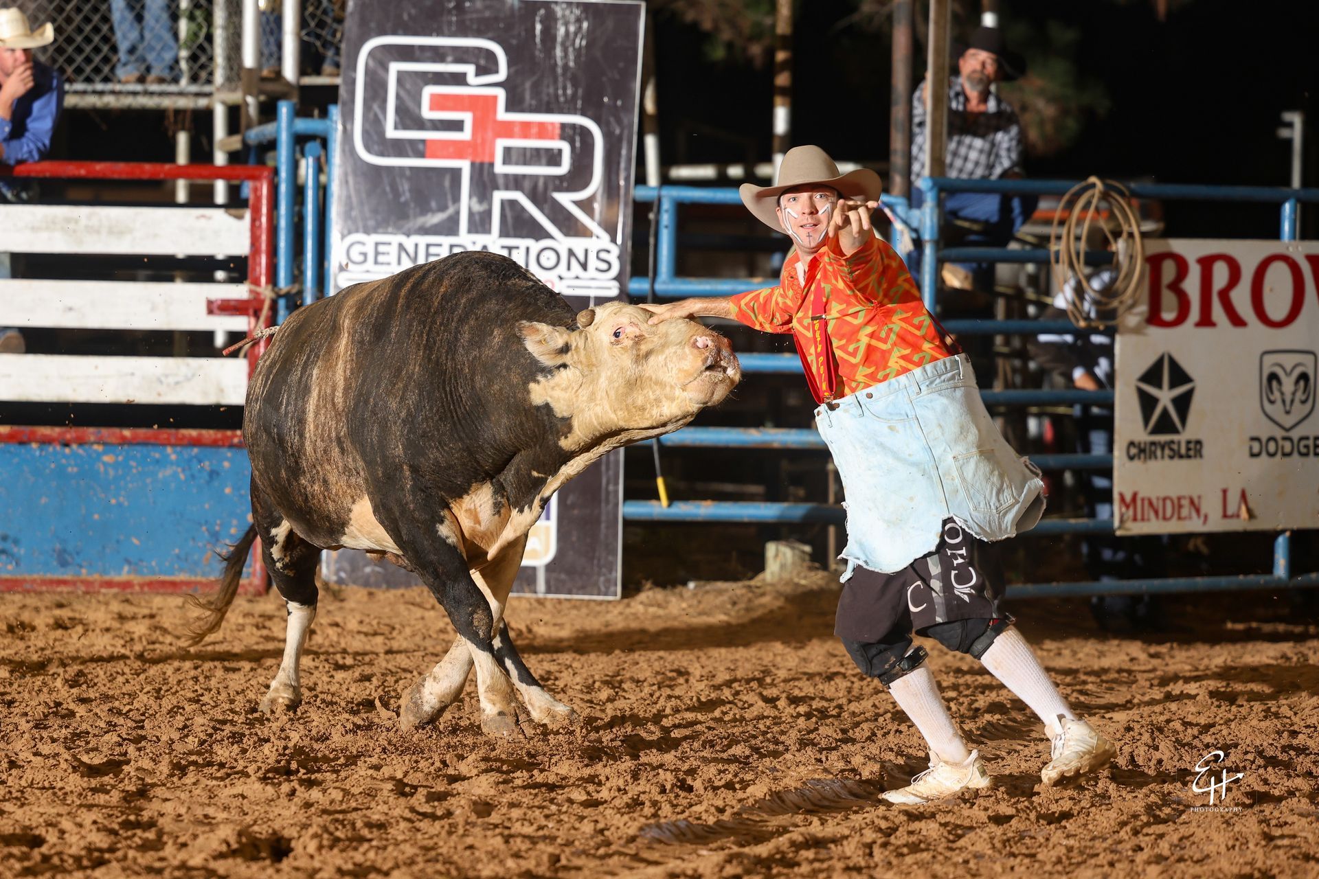 Cowboy in orange shirt and white chaps dodges a bucking bull in a rodeo arena