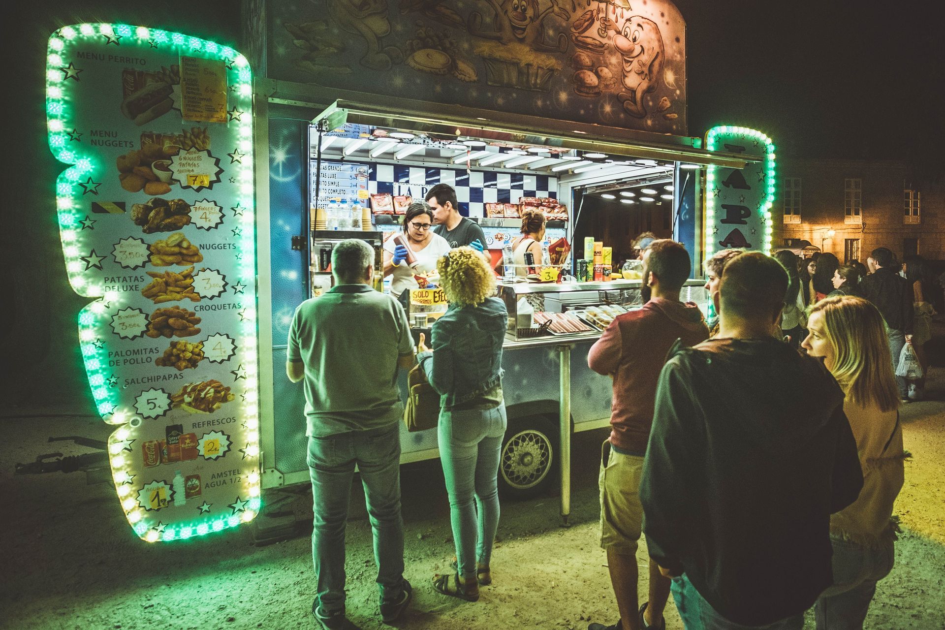 Night food truck with neon lights, serving customers at a lively outdoor street market.