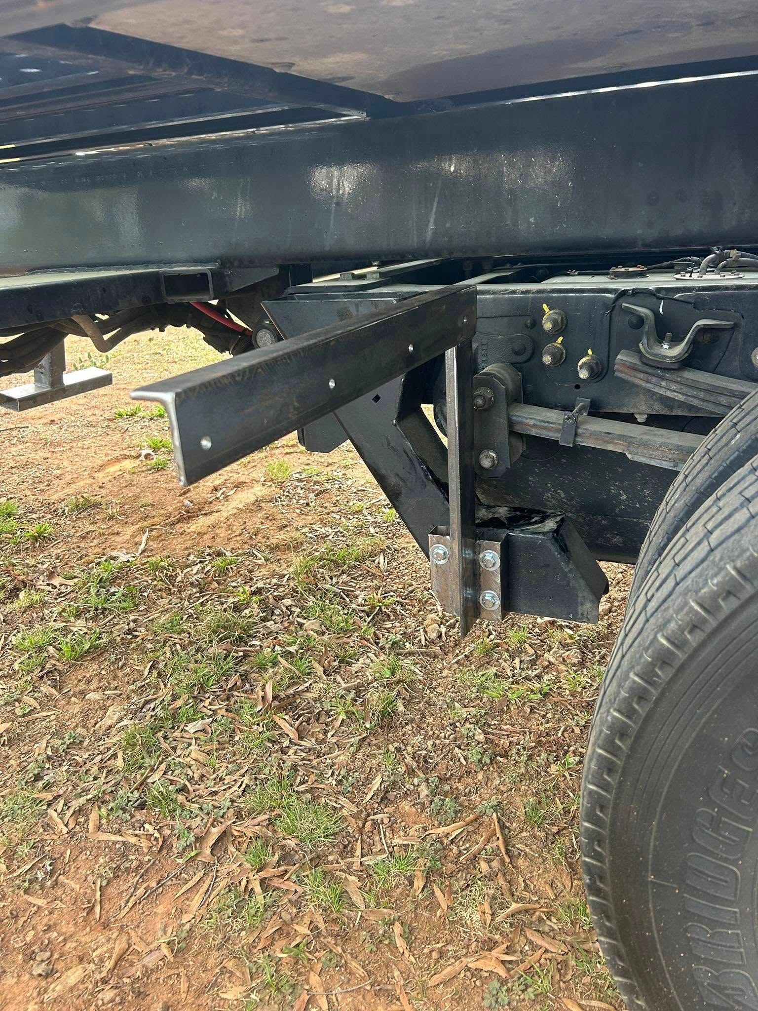 Black metal truck bed support bracket extending beside a wheel on grass and gravel