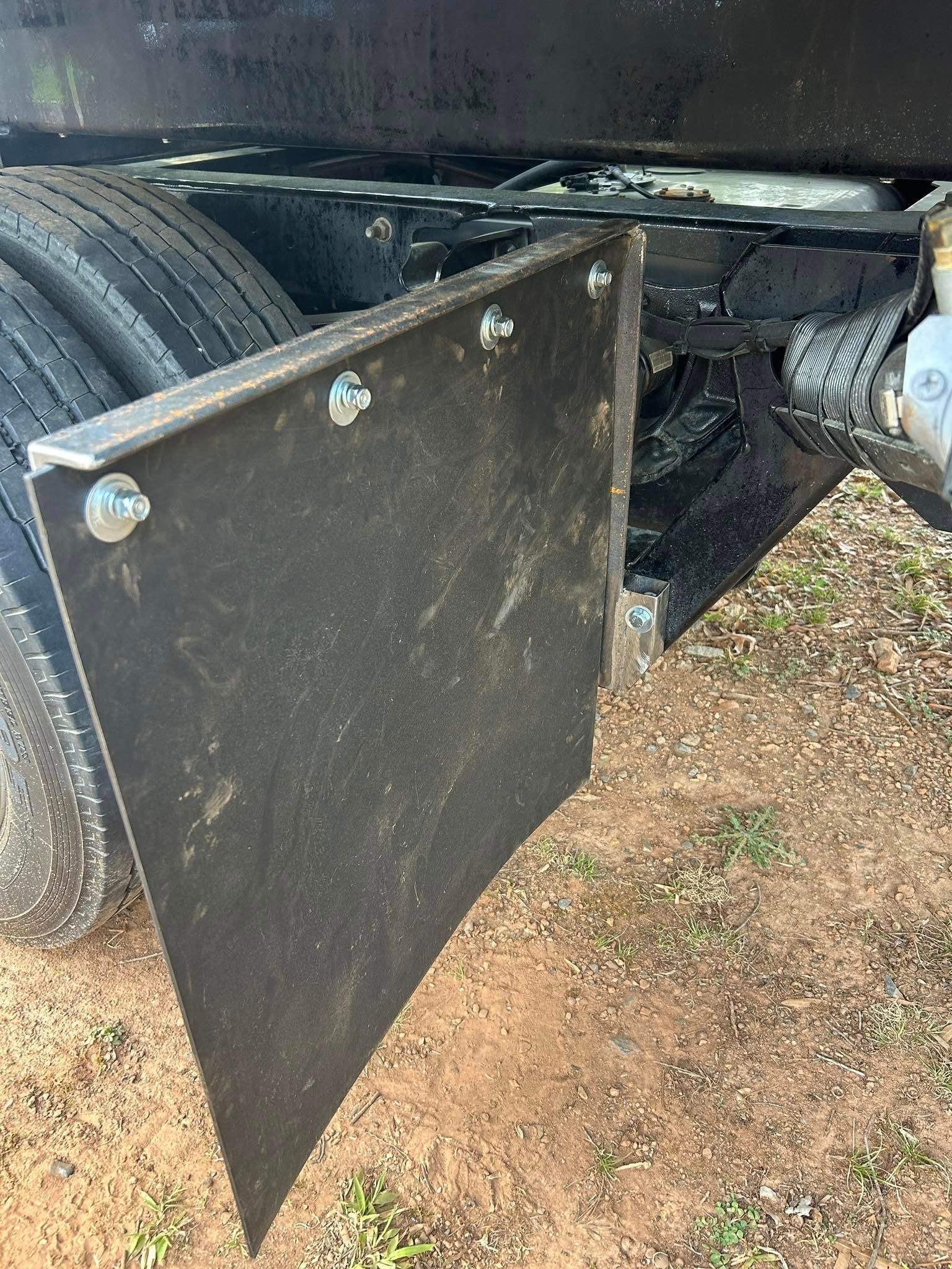 Black metal trailer side panel open beside a tire on dirt ground