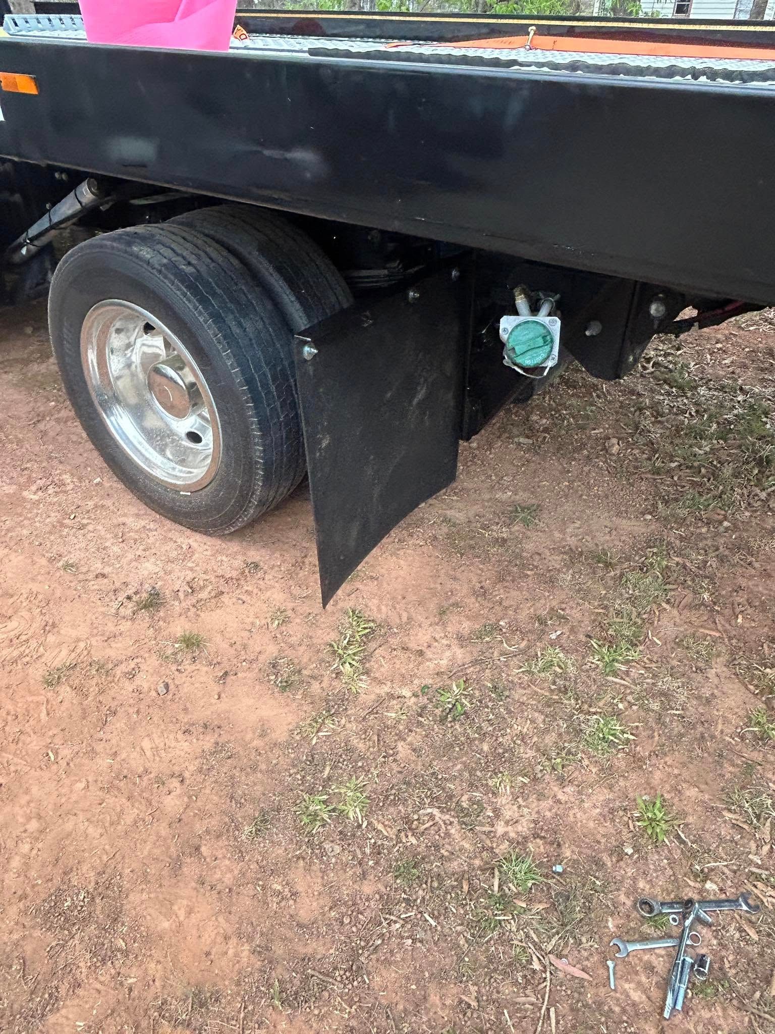Black trailer with a rear wheel and mud flap parked on dirt ground outdoors.