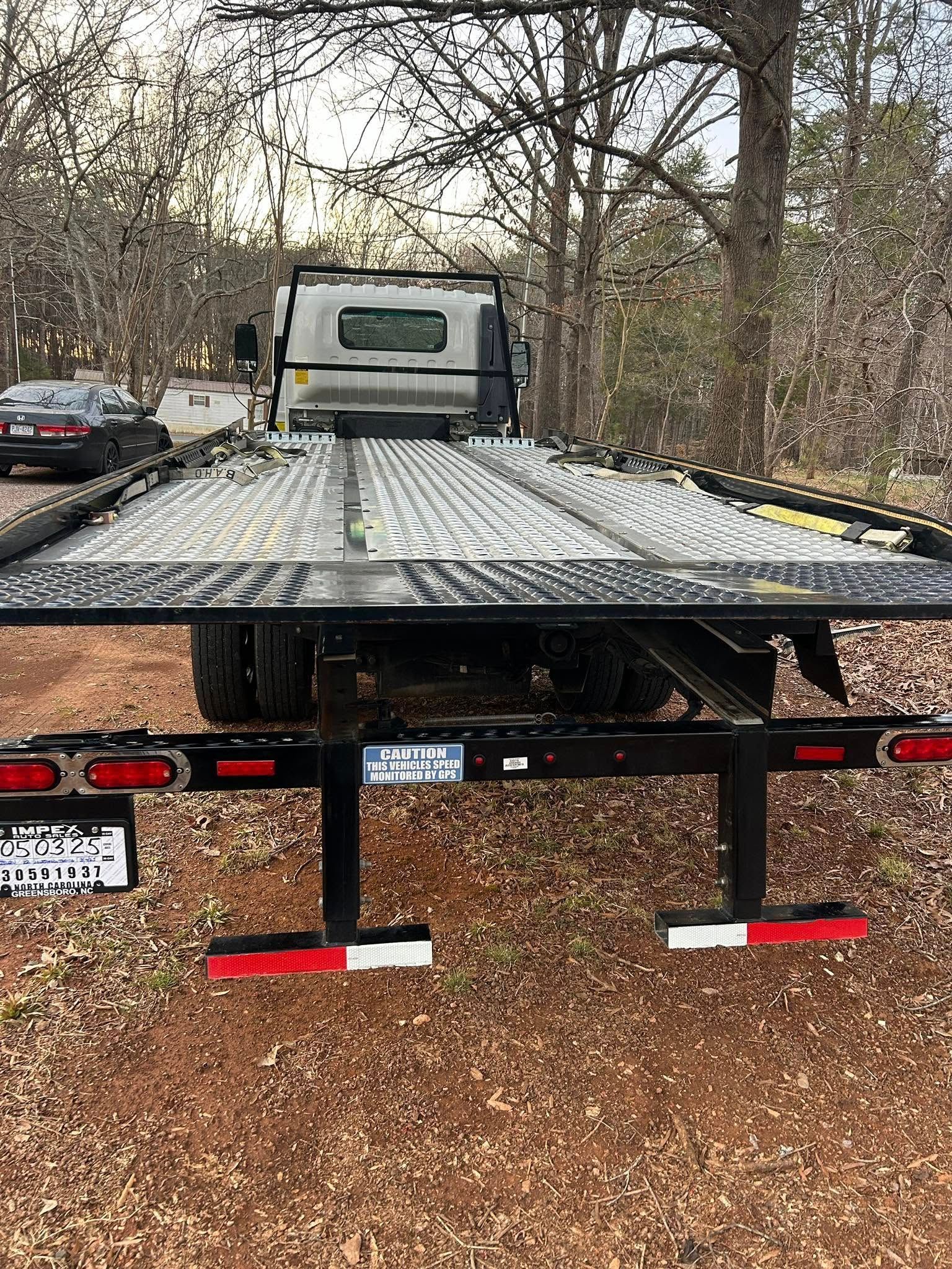 Flatbed tow truck with a silver cab parked on a snowy road lined with trees.