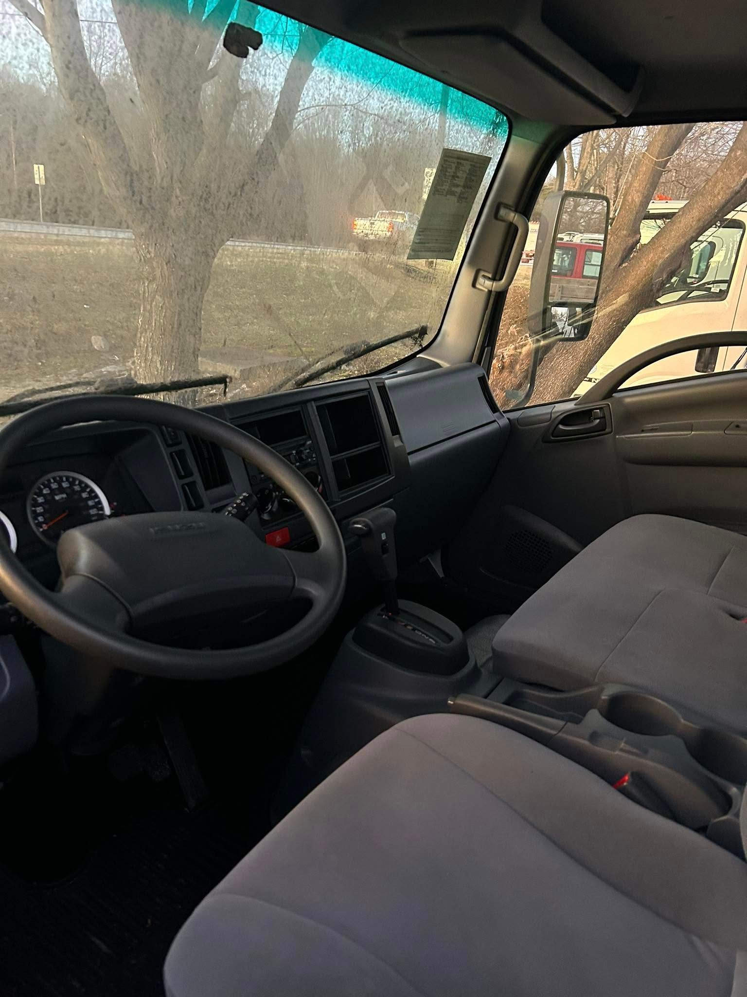 Car interior with black dashboard and gray seats, showing the steering wheel and passenger seat by a window.