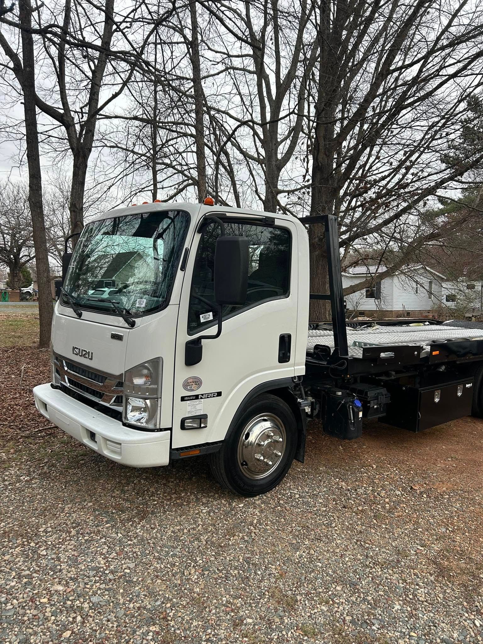 White flatbed truck parked on gravel under leafless trees in an overcast setting