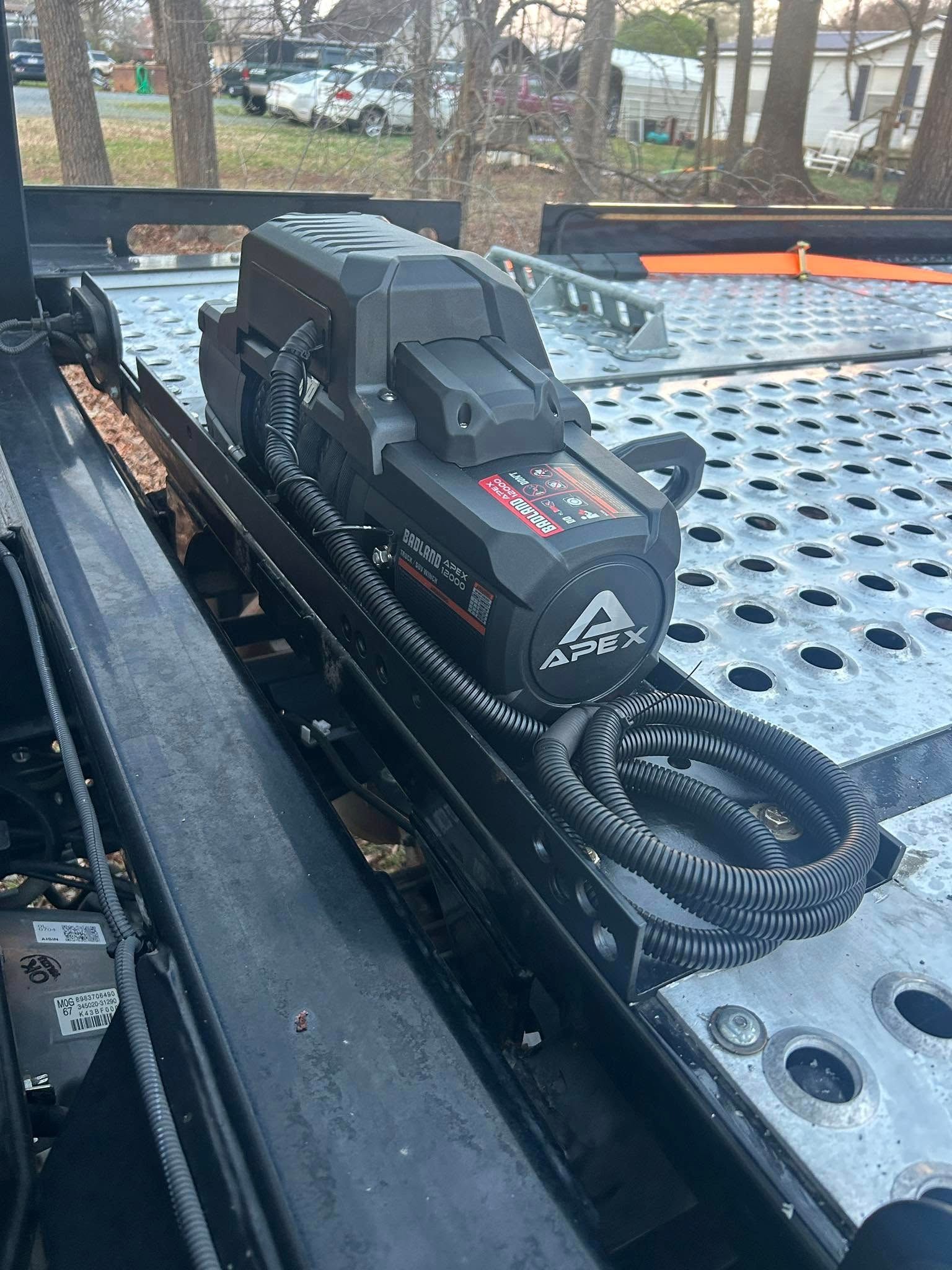 Black device with coiled cable mounted on a perforated metal surface in a vehicle bed