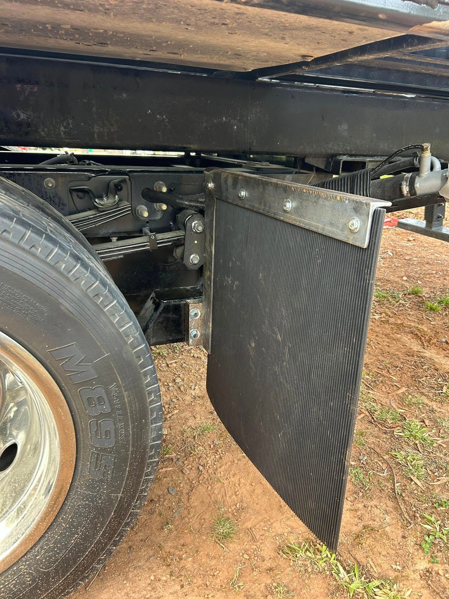 Black rubber mud flap hanging behind a truck wheel on a gravel surface