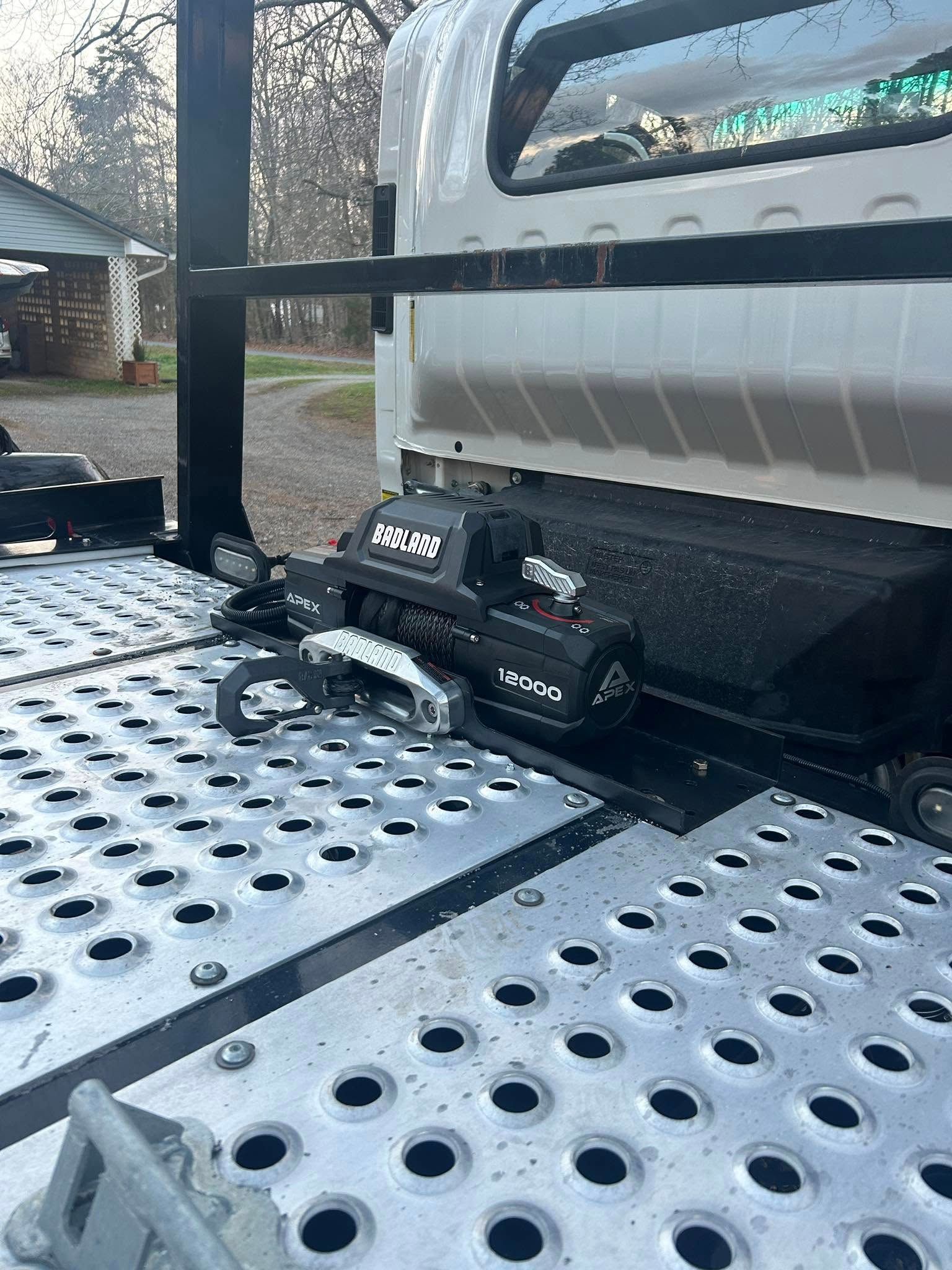 Black RC truck on a perforated metal trailer bed beside a white vehicle.