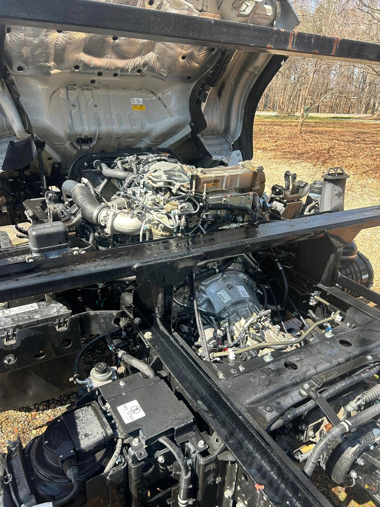 Burned vehicle engine compartment with exposed mechanical parts and charred frame under an open hood