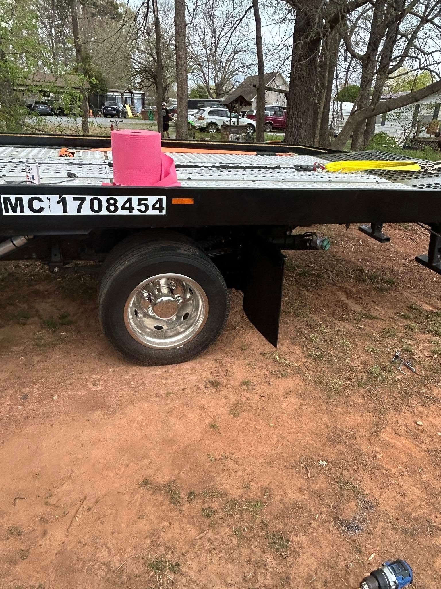 Flatbed trailer with a white and red box on top, parked on dirt under trees.