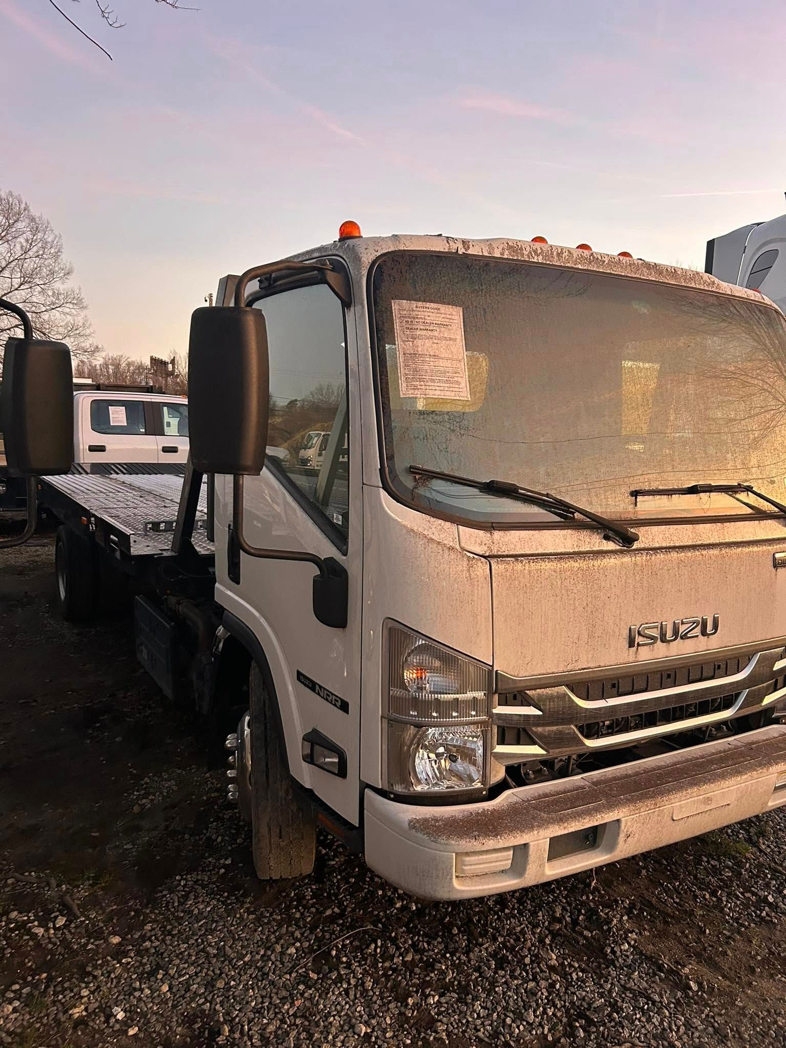 White Isuzu truck parked on a wet gravel lot at sunrise, with another truck behind it.