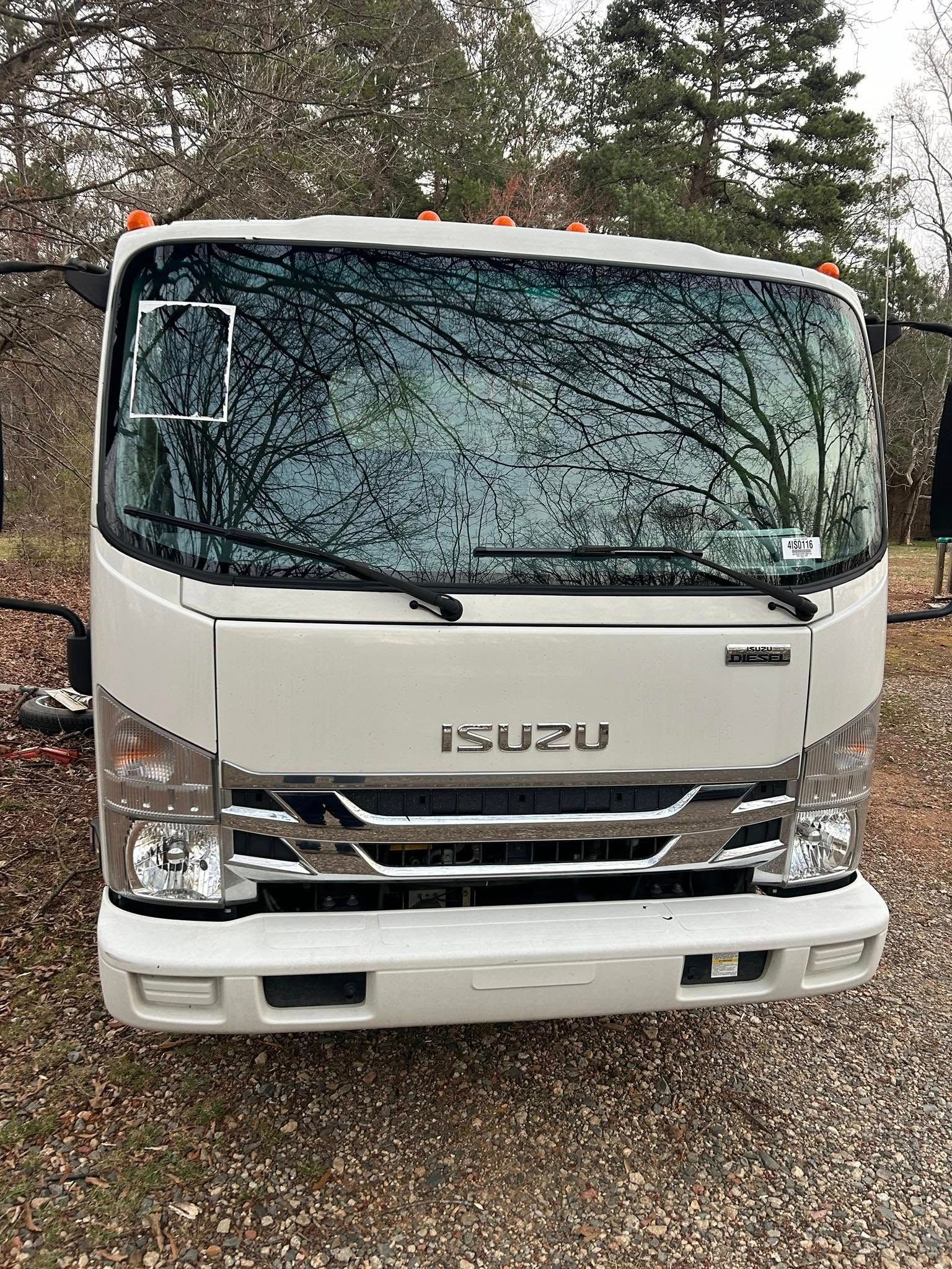 Front view of a white Isuzu truck parked outdoors on gravel, with trees in the background