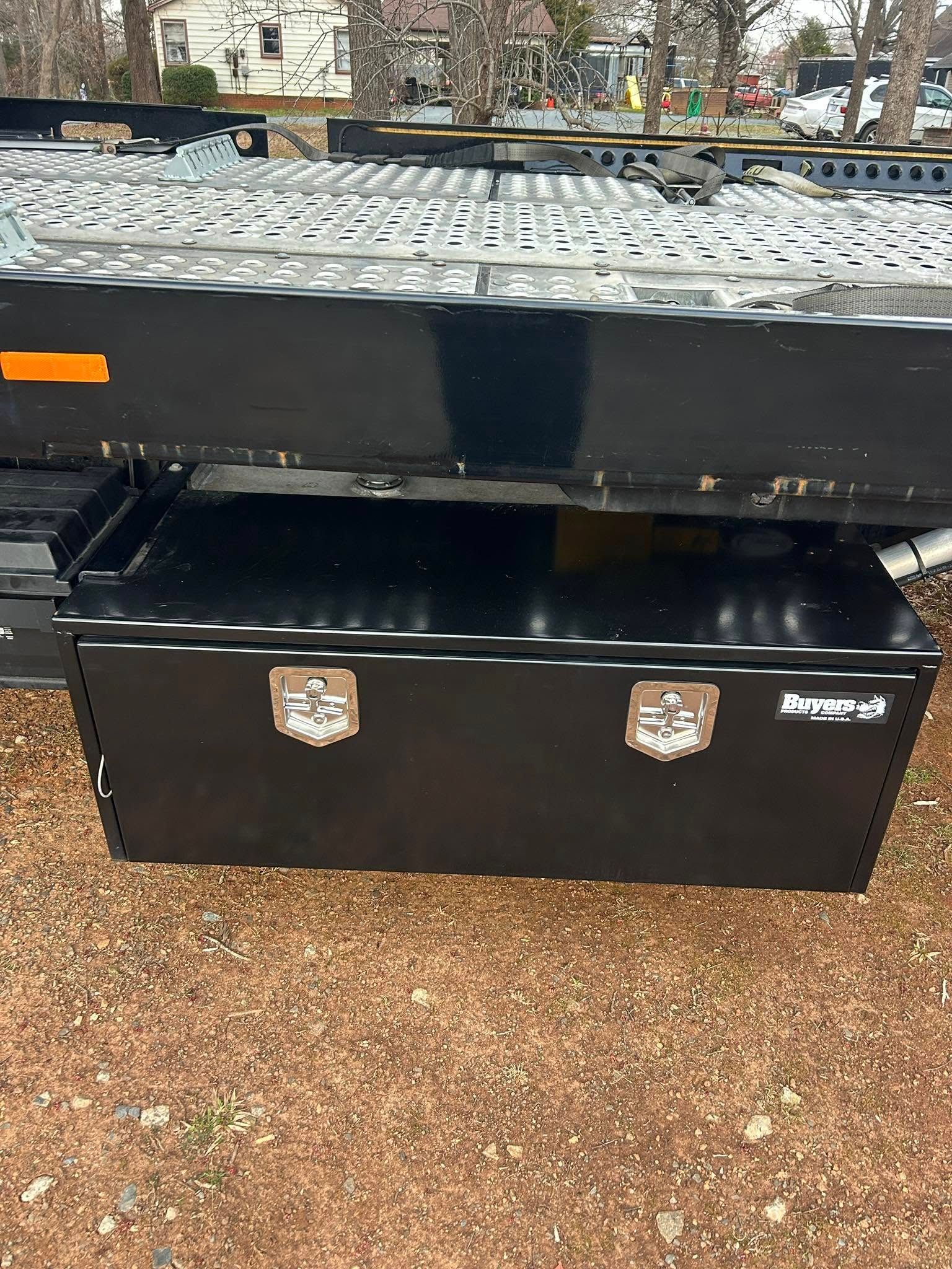 Black metal utility trailer with reflective tape, parked on gravel outdoors