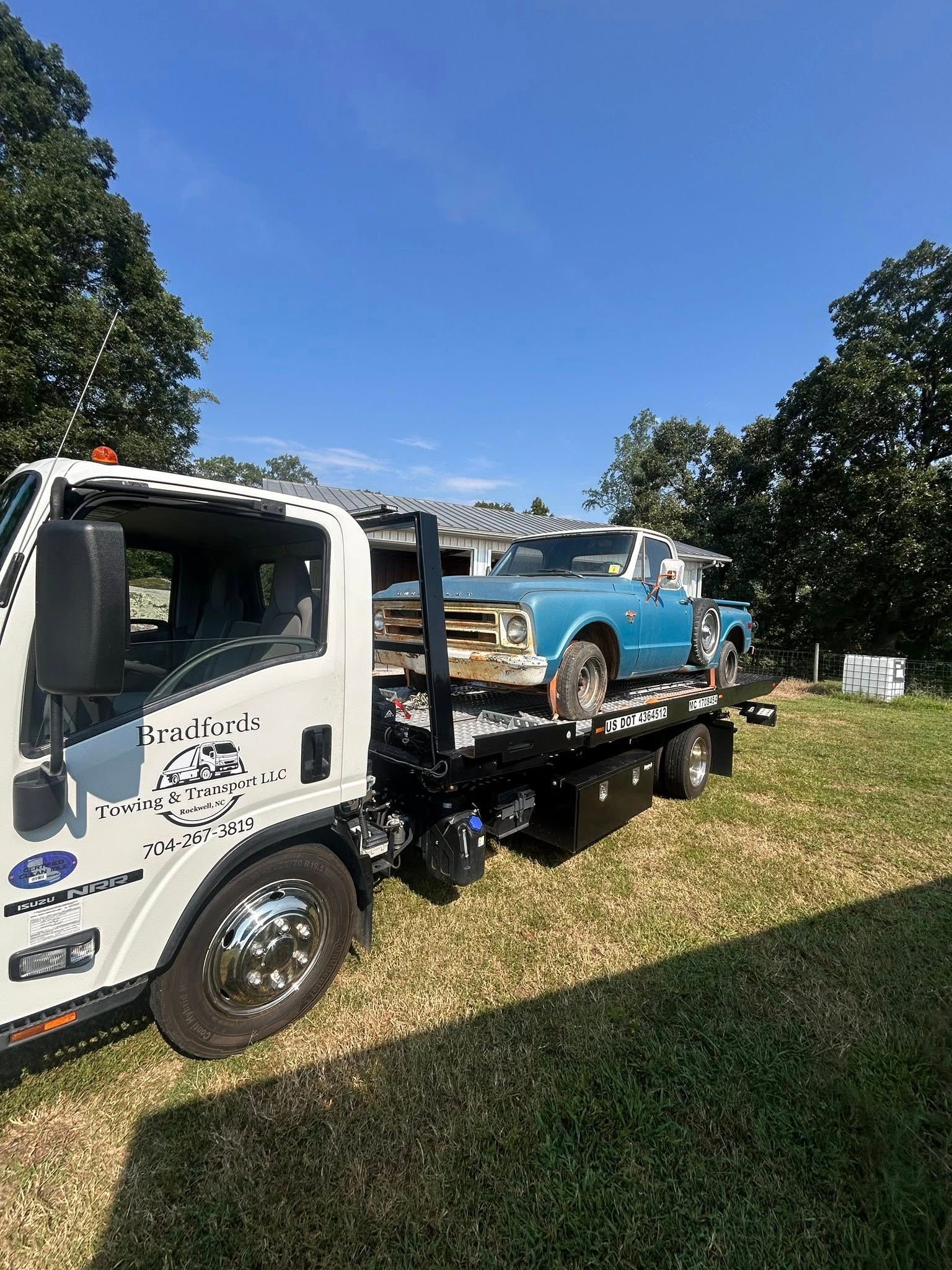 Blue vintage car on a flatbed tow truck in a grassy field under a clear sky