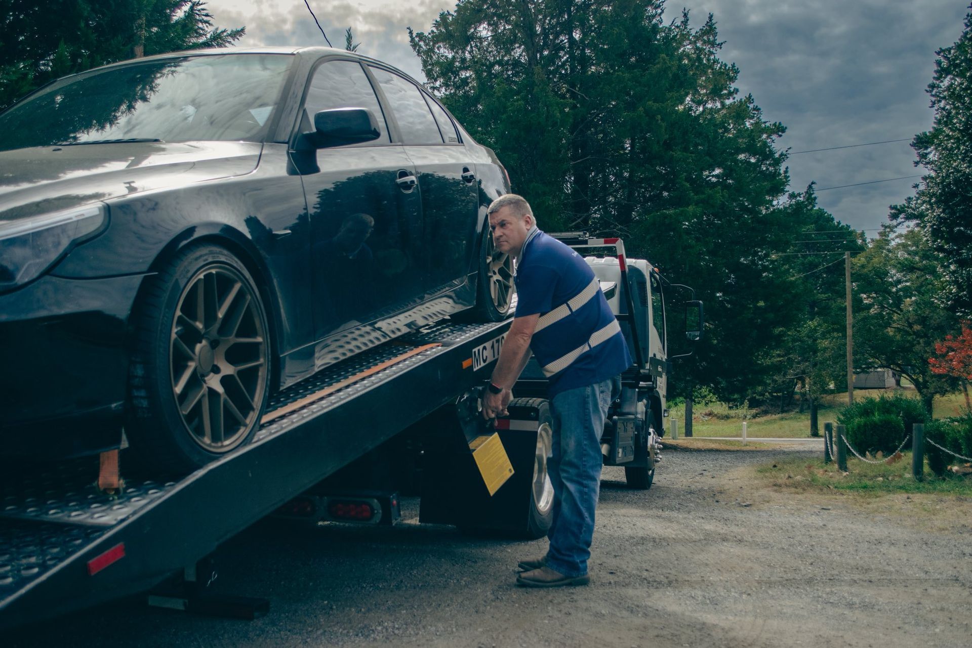 Tow truck loading a black car while a man steadies it on a roadside driveway