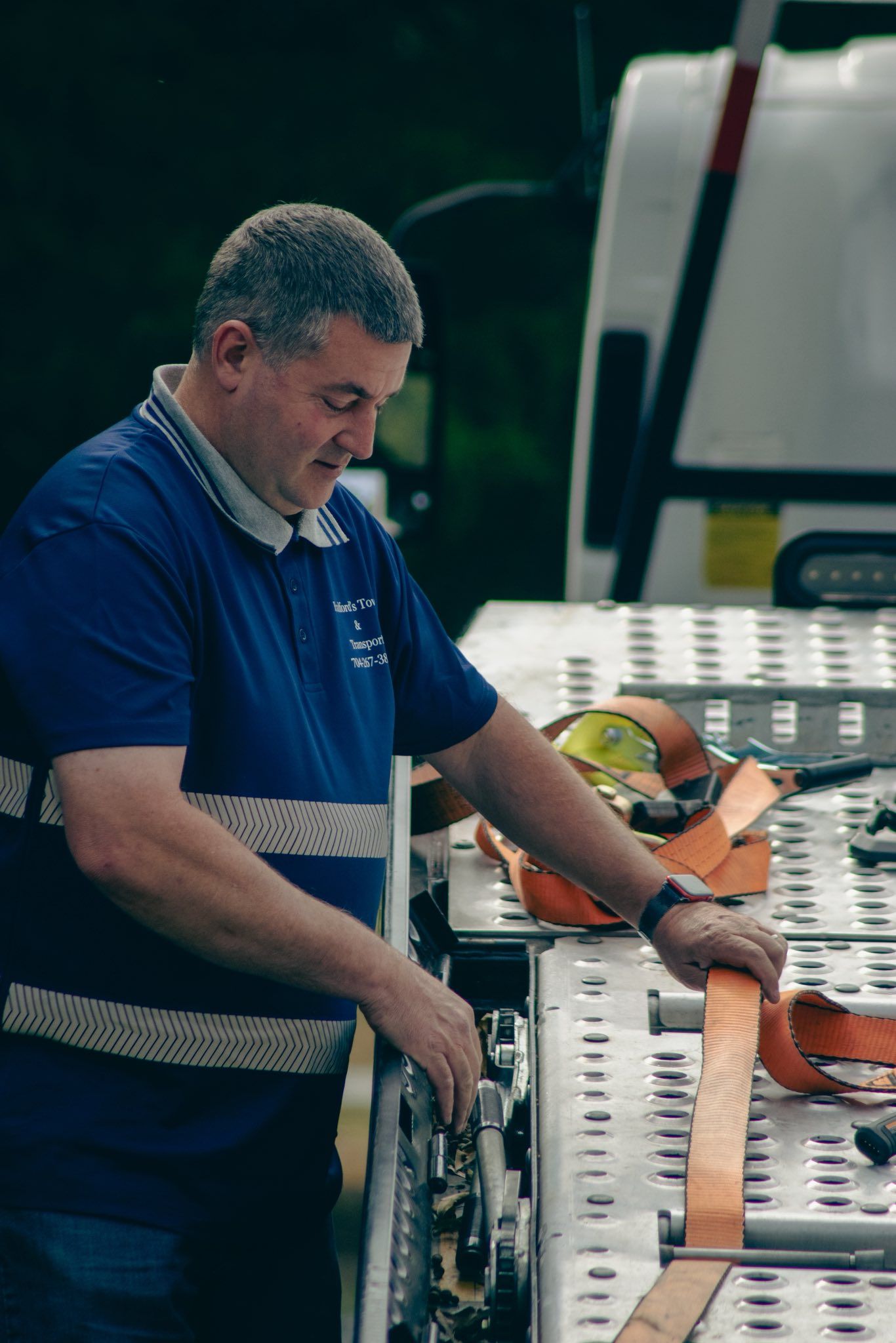 Man in blue shirt securing orange straps on equipment in a work vehicle