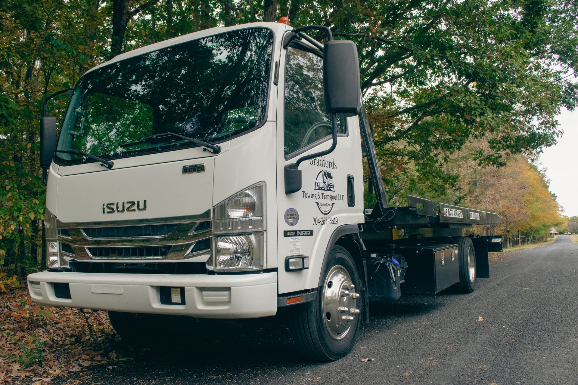 White Isuzu flatbed truck parked on a tree-lined road