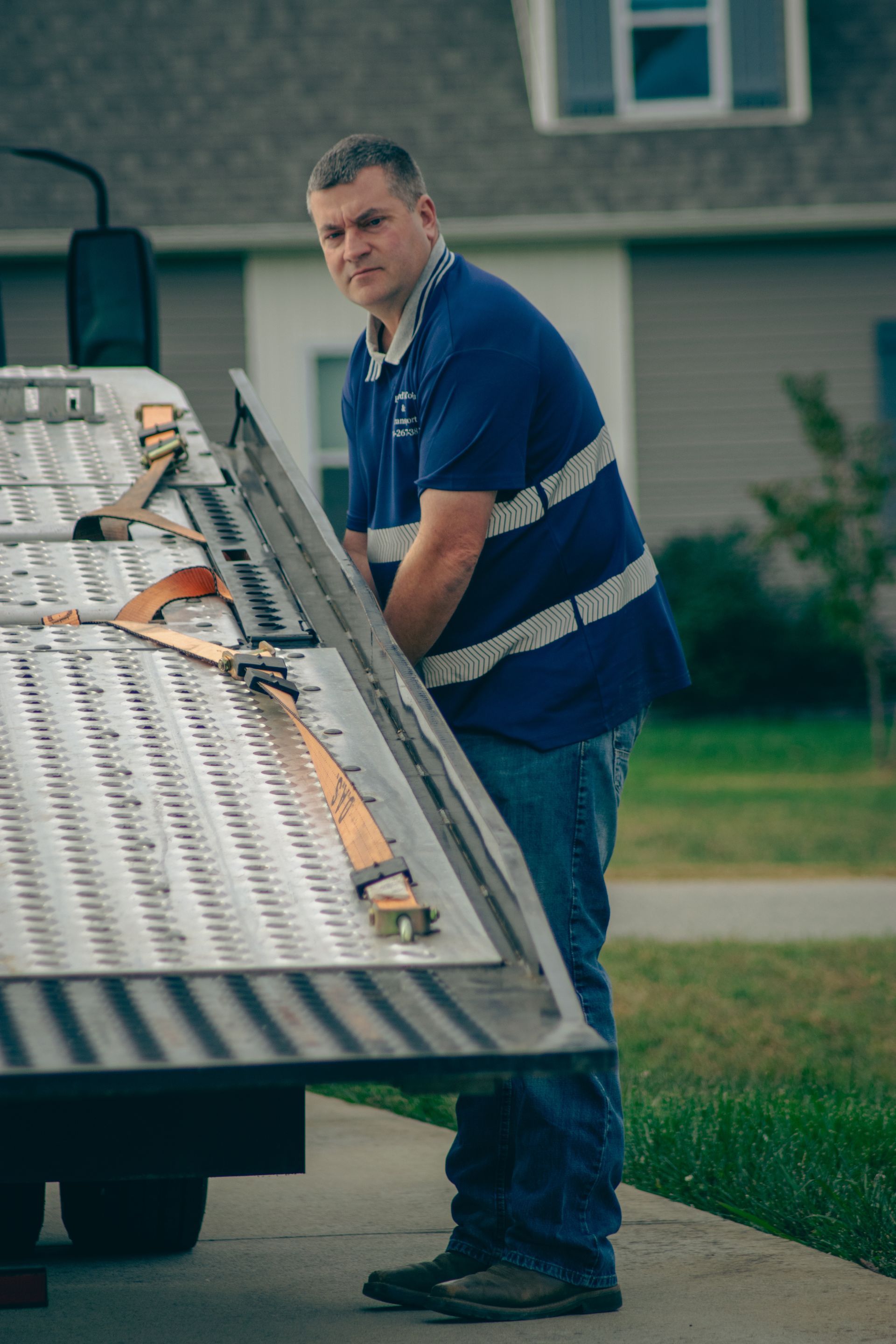 Man in blue shirt lifting a ladder from a roof rack in a suburban driveway