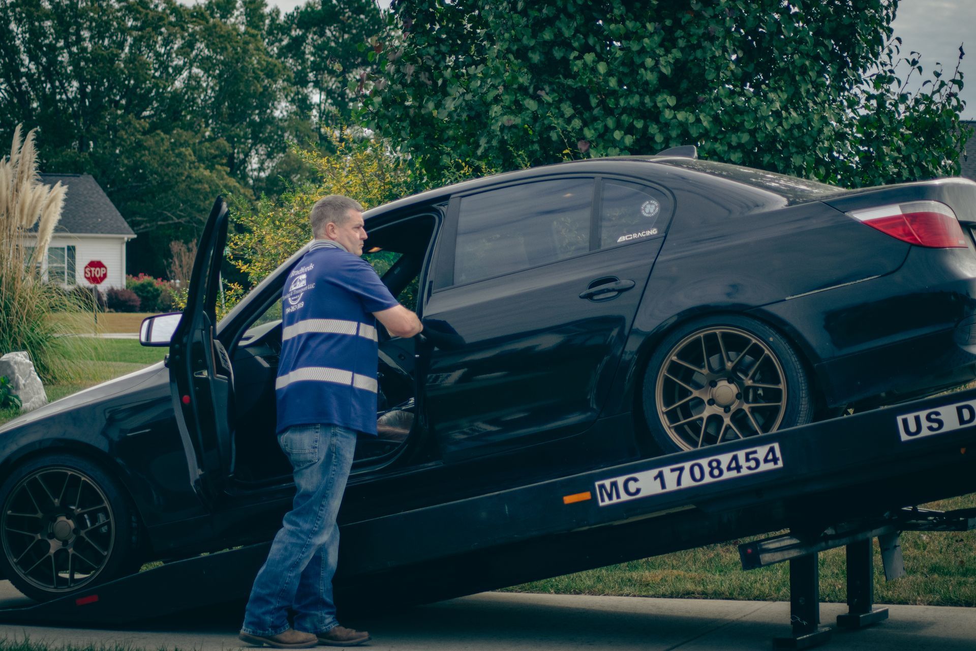 Tow truck driver loading a black sedan onto a flatbed on a suburban street