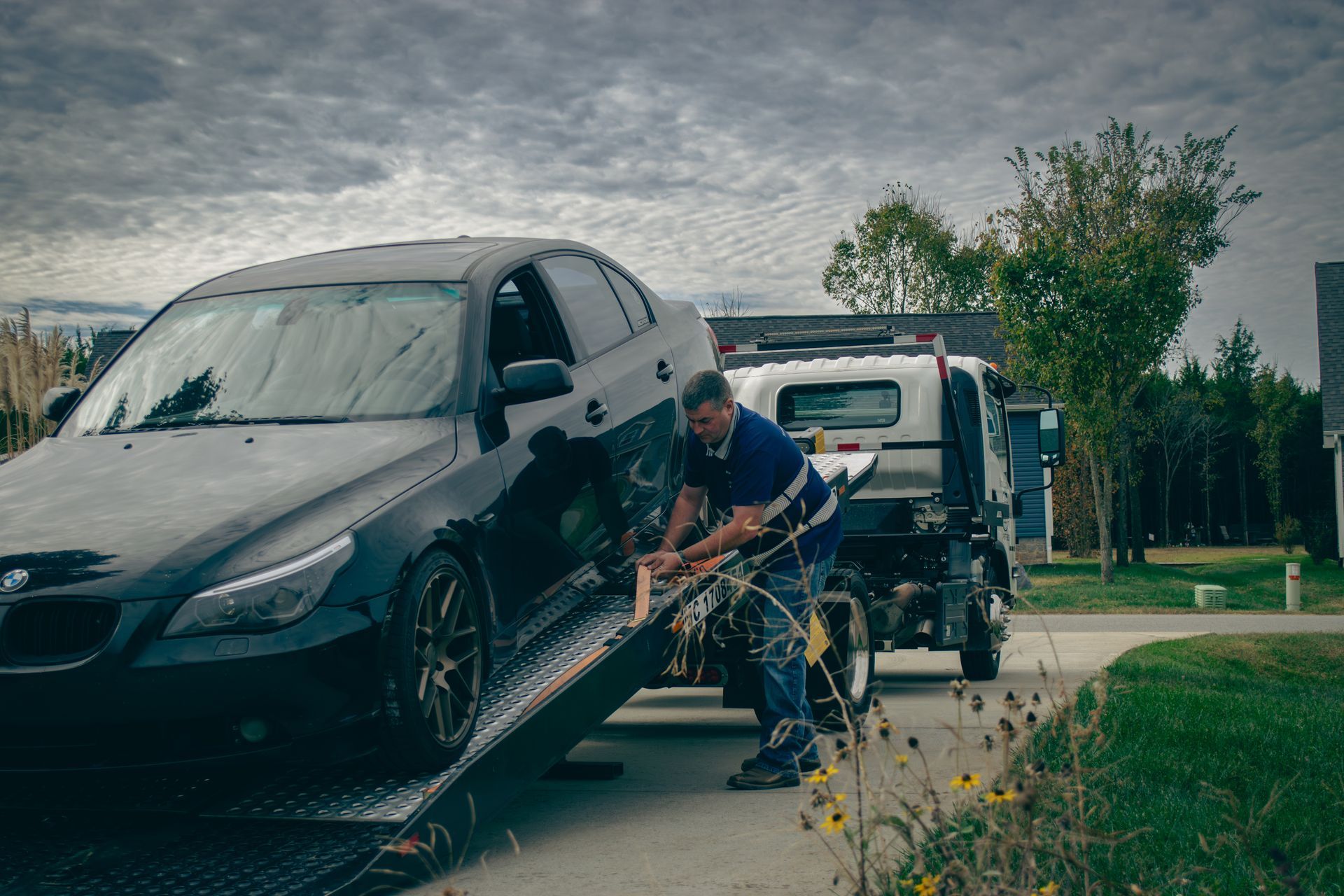 Tow truck operator loading a black car onto a flatbed truck on a roadside