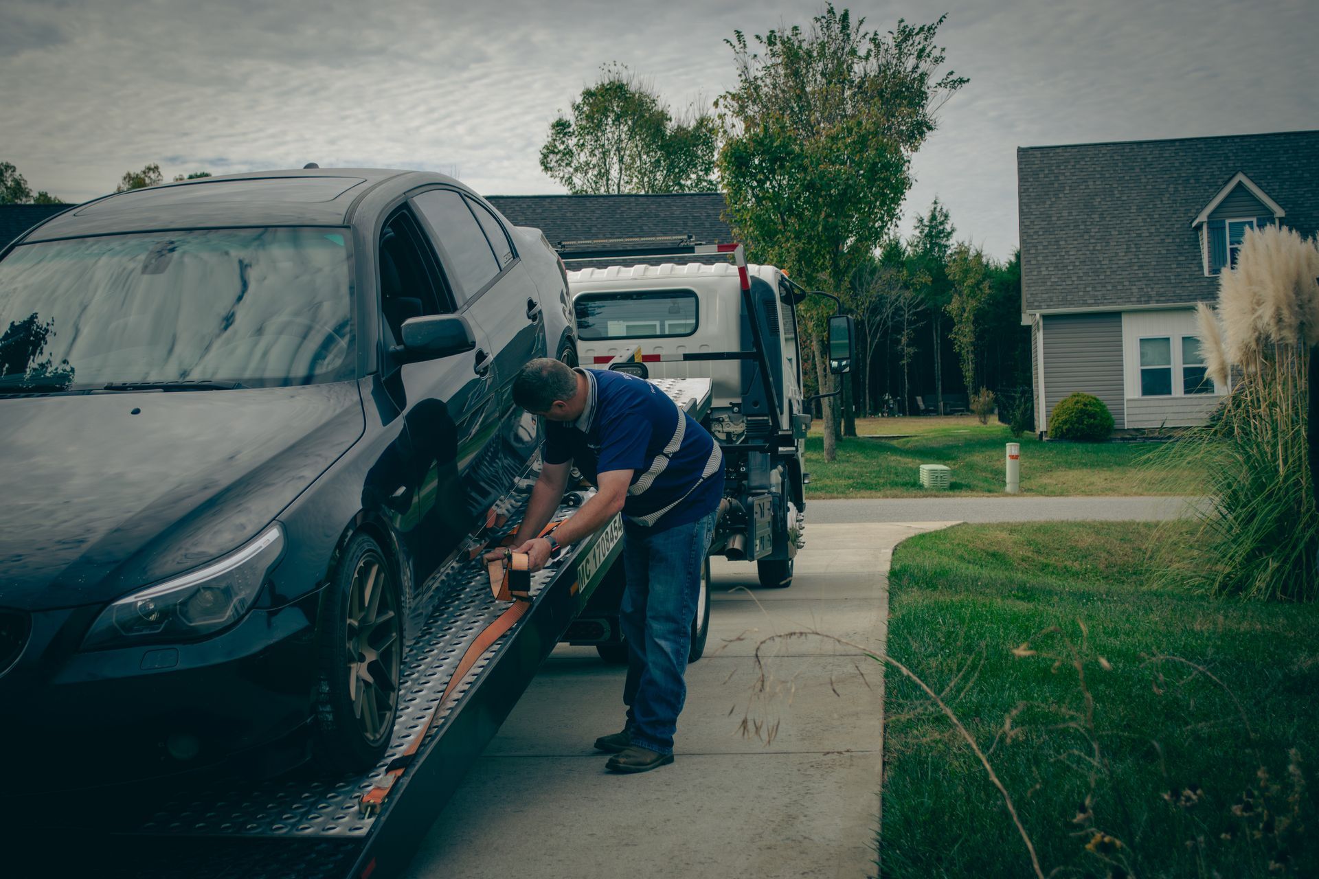 Tow truck worker loading a black SUV on a driveway in a suburban neighborhood