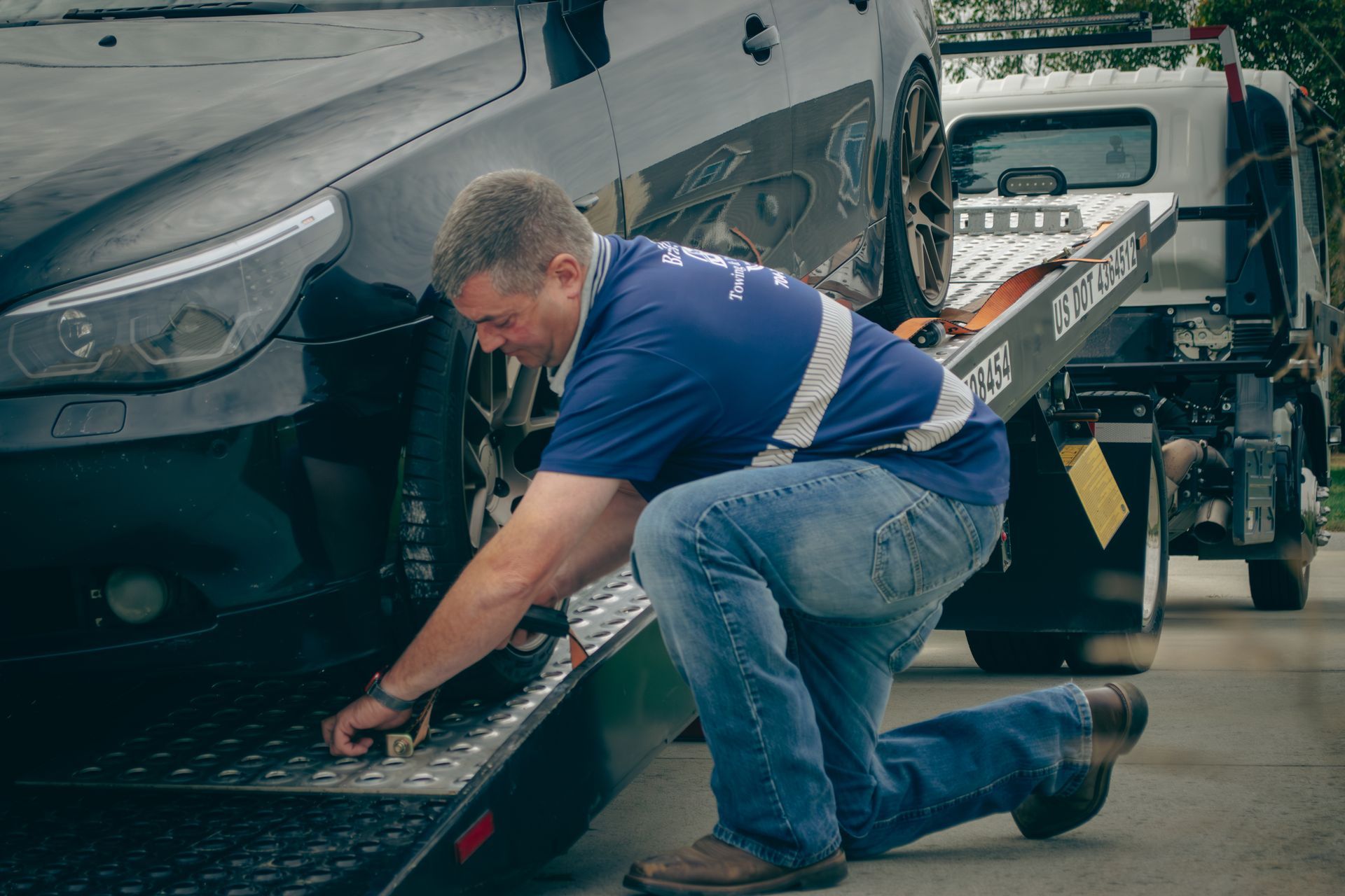 Tow truck operator securing a black car onto a flatbed in a roadside recovery scene