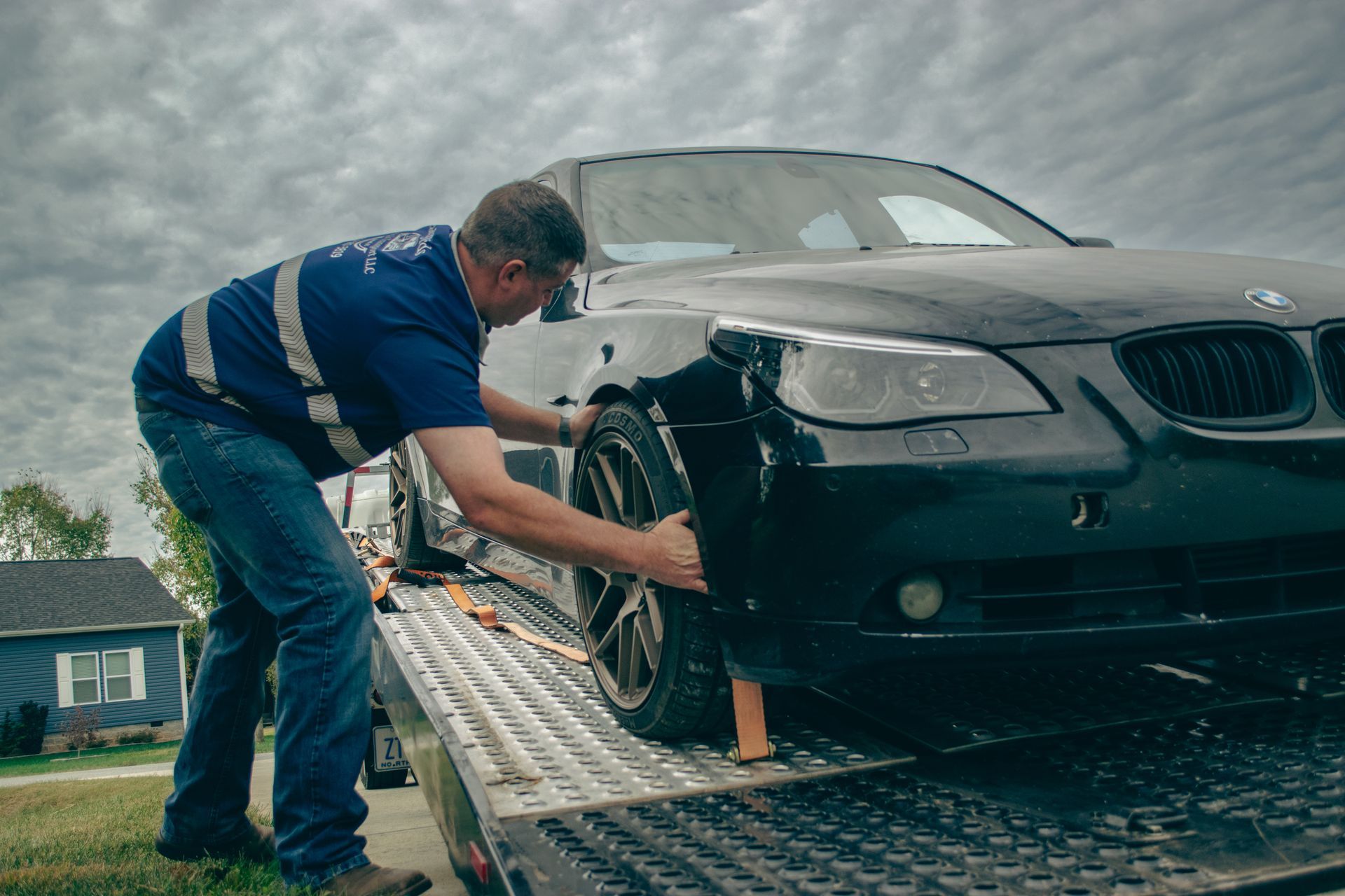 Tow truck driver loading a black BMW onto a flatbed in the rain