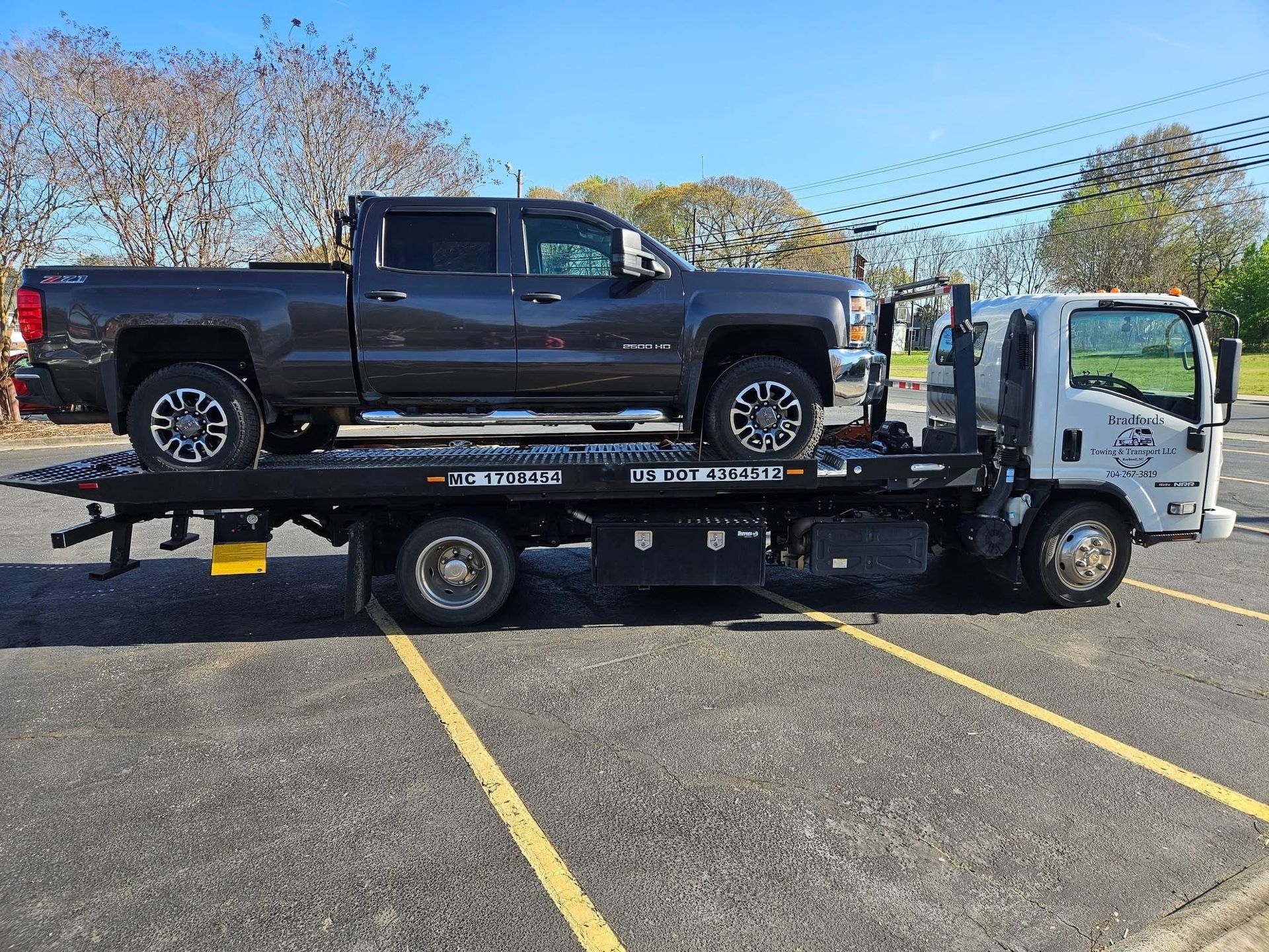 Black pickup on a flatbed tow truck in a parking lot under a clear sky