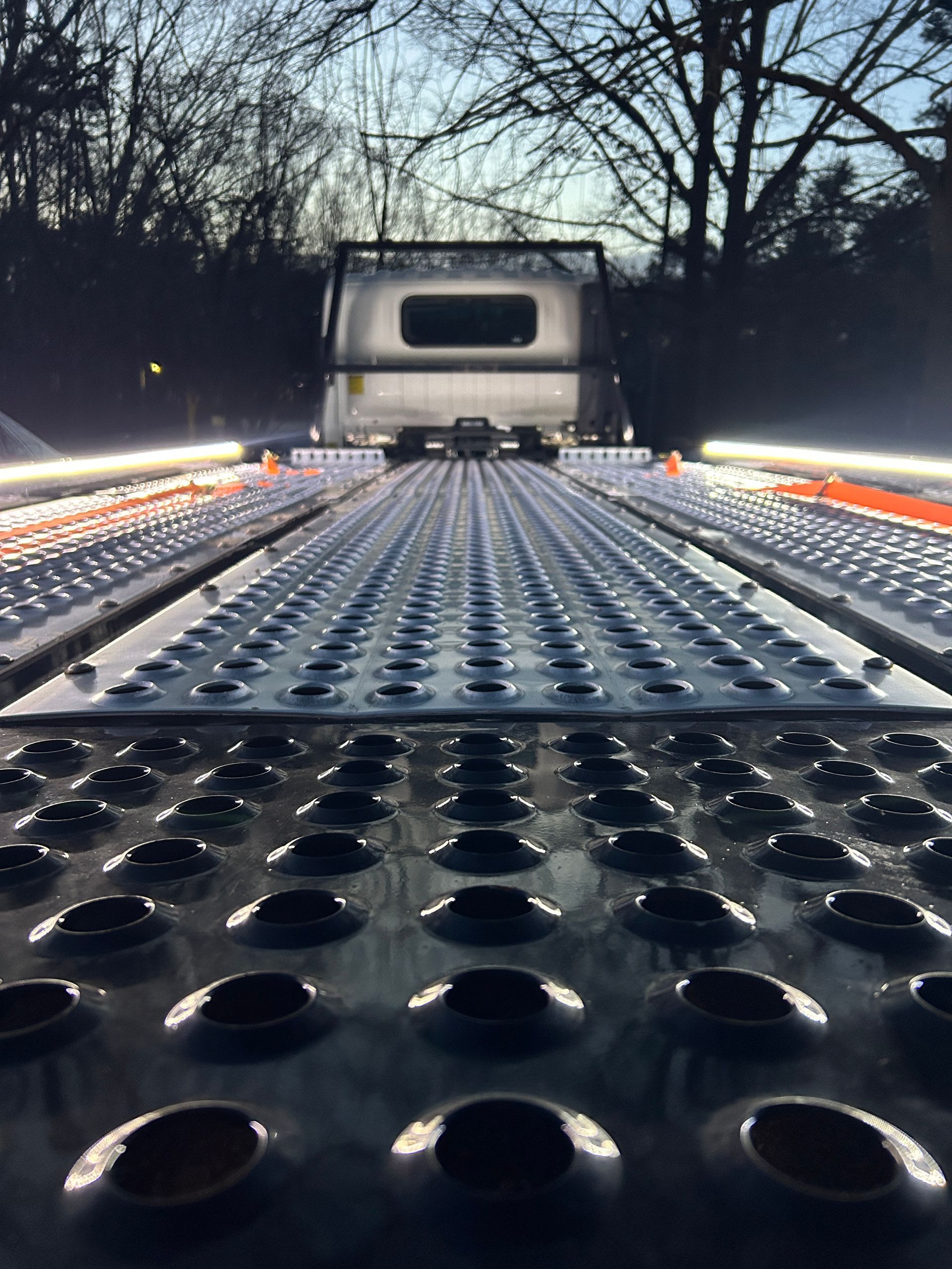 Perforated truck flatbed seen from the rear at dusk, with bare trees silhouetted in the background