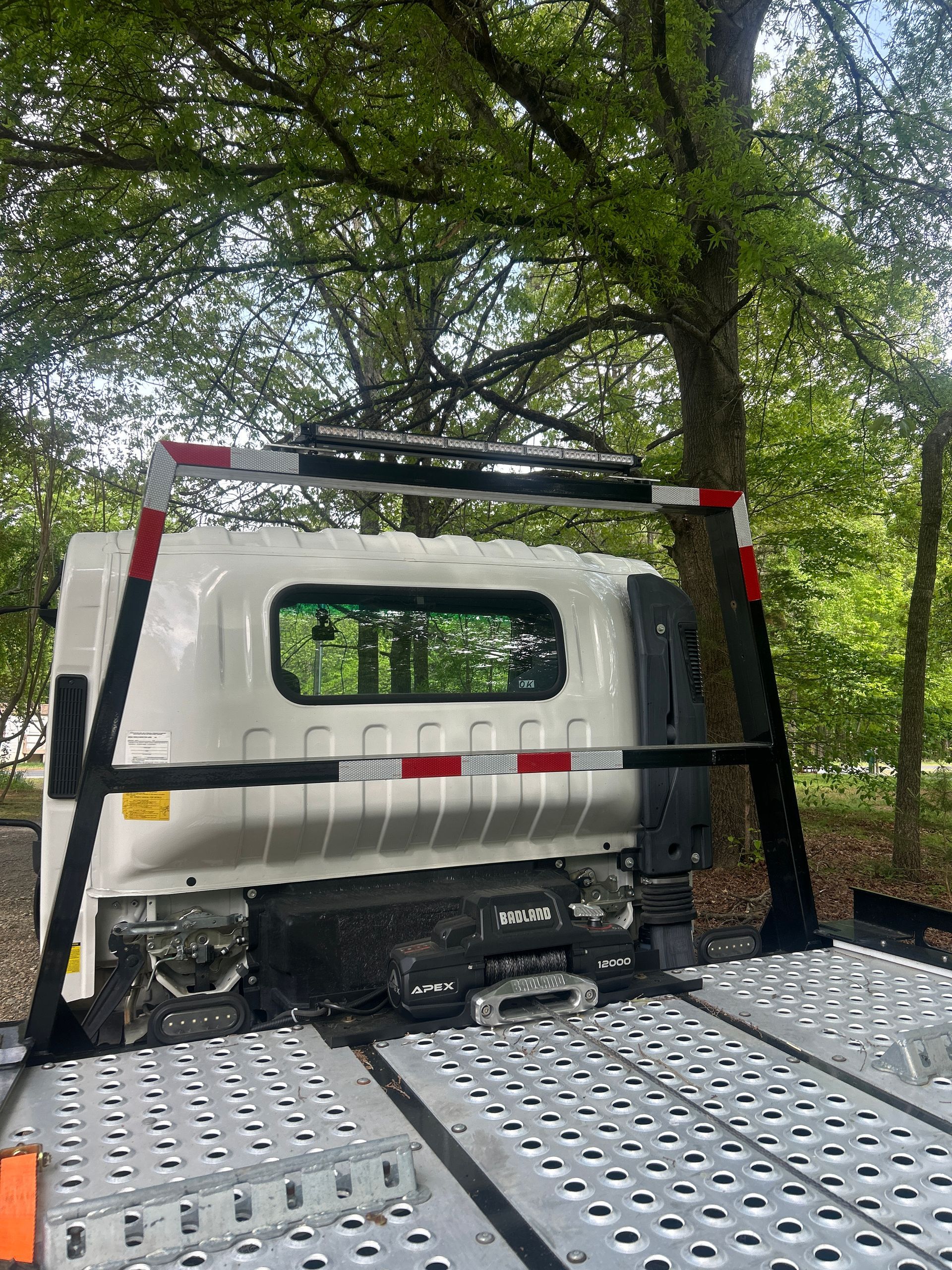 White van on a tow truck bed under trees, seen from the rear.