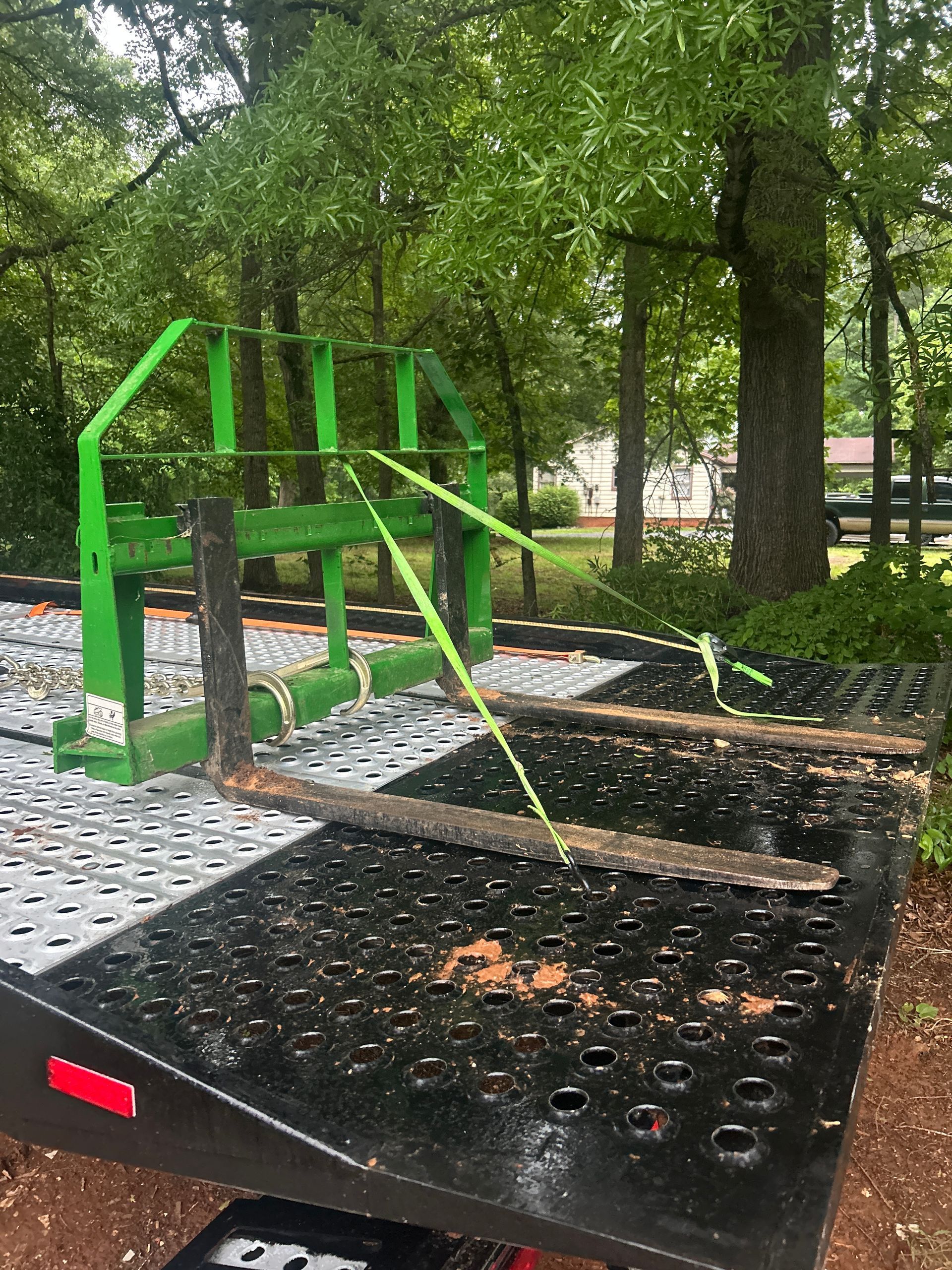 Green metal playground climbing structure with ramps and steps in a shaded park