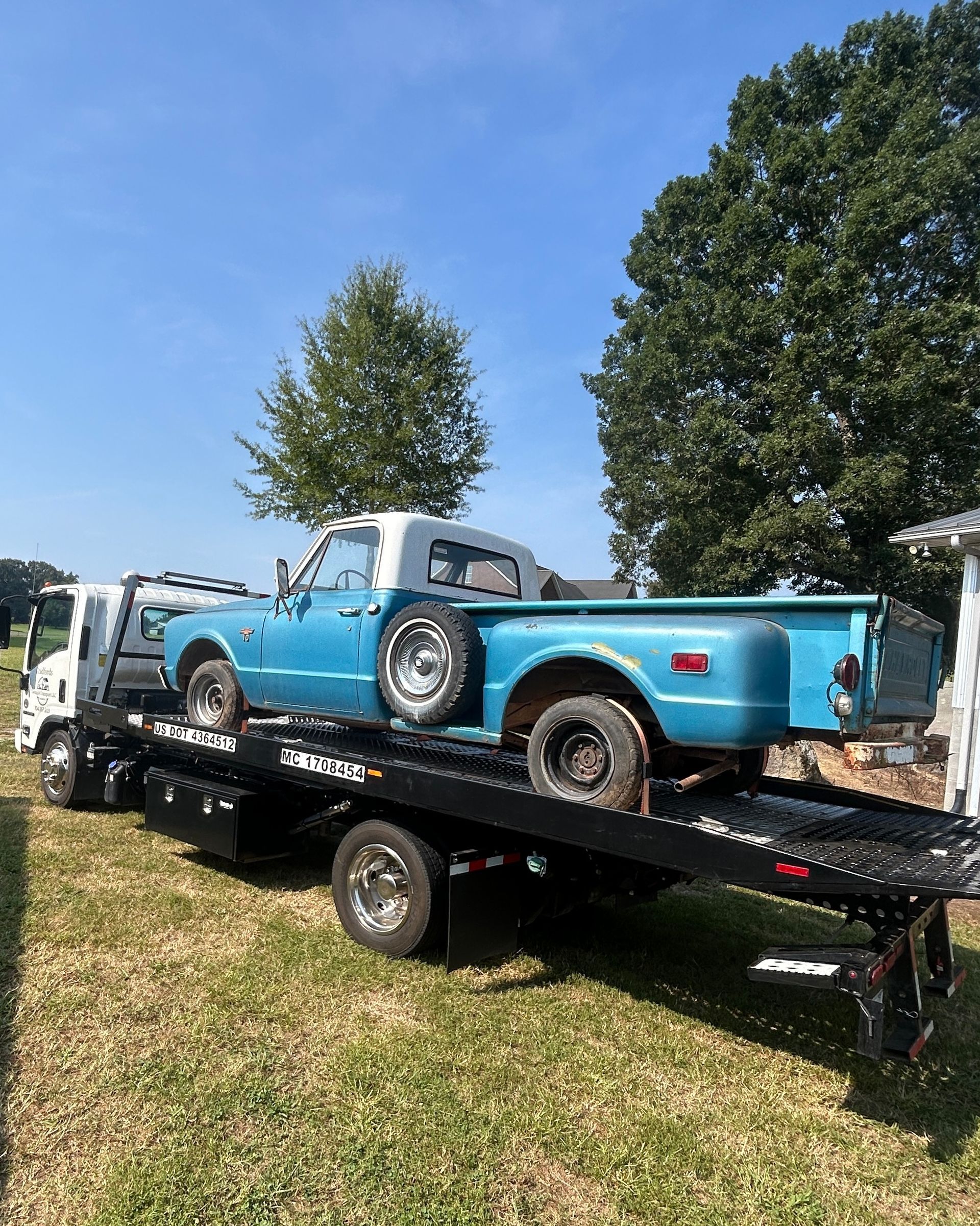 Blue vintage pickup truck on a black trailer in a grassy yard under a clear sky