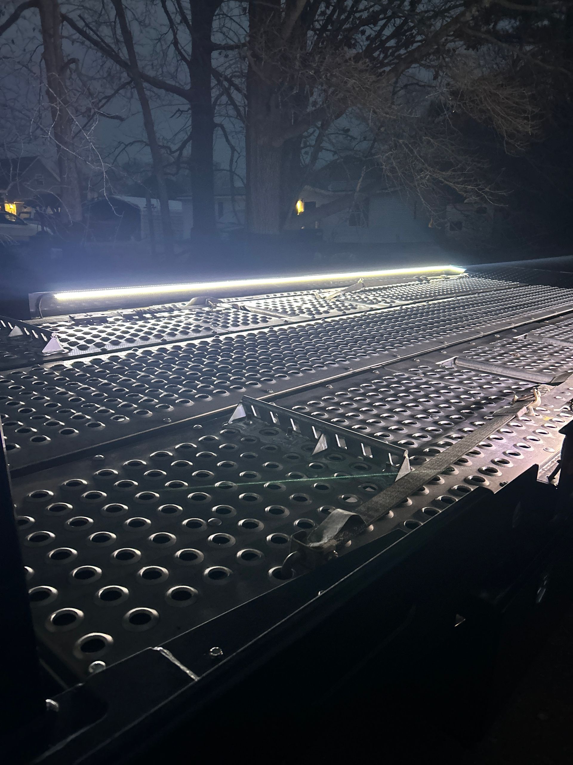 LED light bar illuminating a perforated metal platform at night in a wooded area