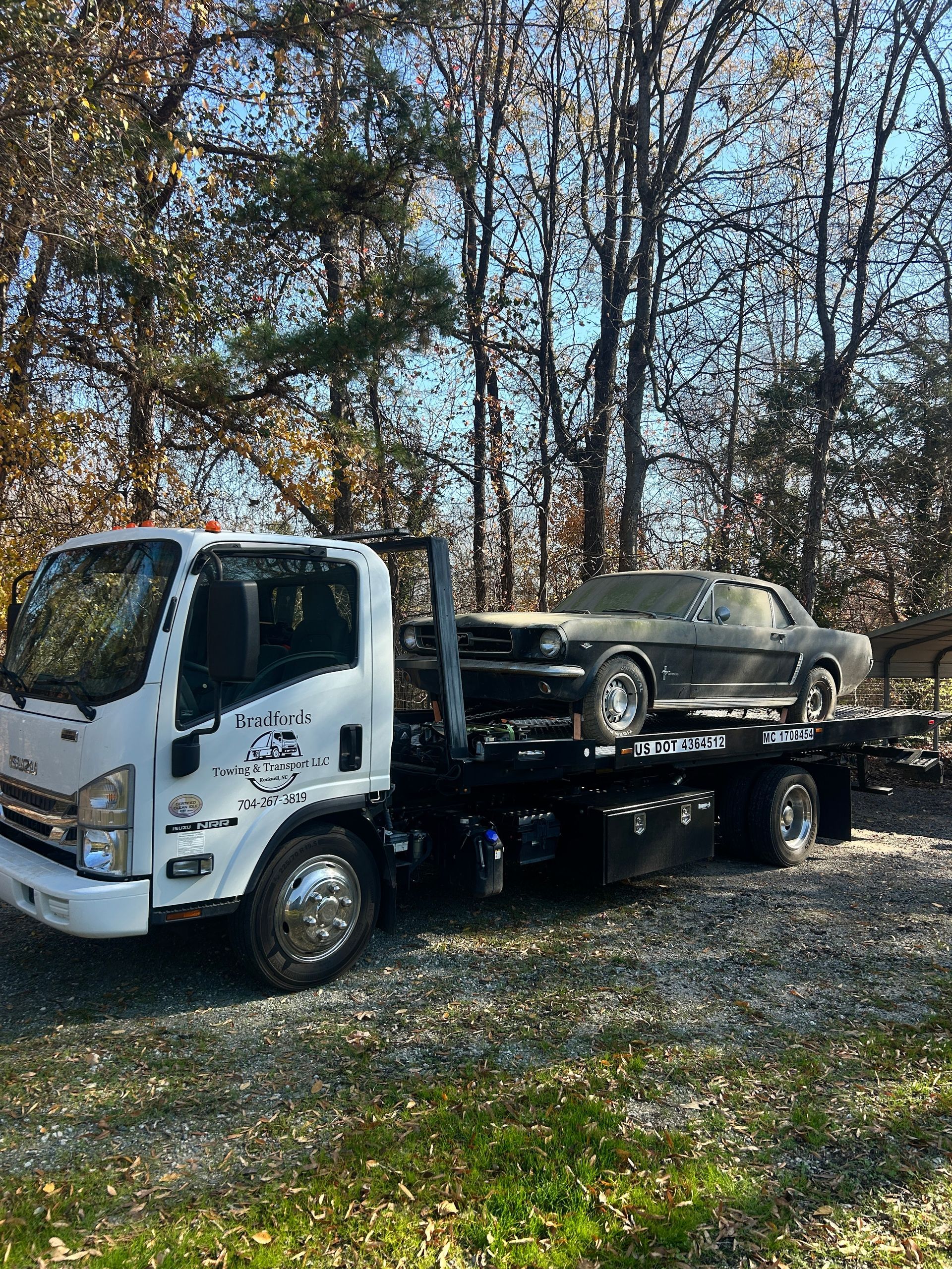 Tow truck carrying a black sedan on a flatbed in a wooded area