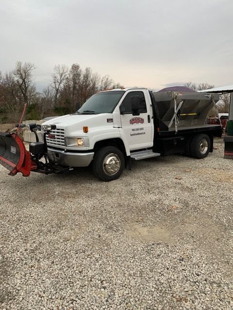 White dump truck with red plow parked on gravel lot under cloudy sky