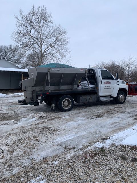 White utility truck with covered bed parked on a snowy driveway beside a building.