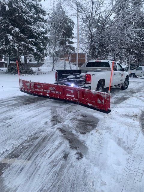 Snowplow truck with red plow clearing a snowy driveway in a winter neighborhood