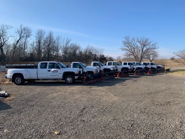 White pickup trucks parked in a row on a gravel lot under a clear blue sky.