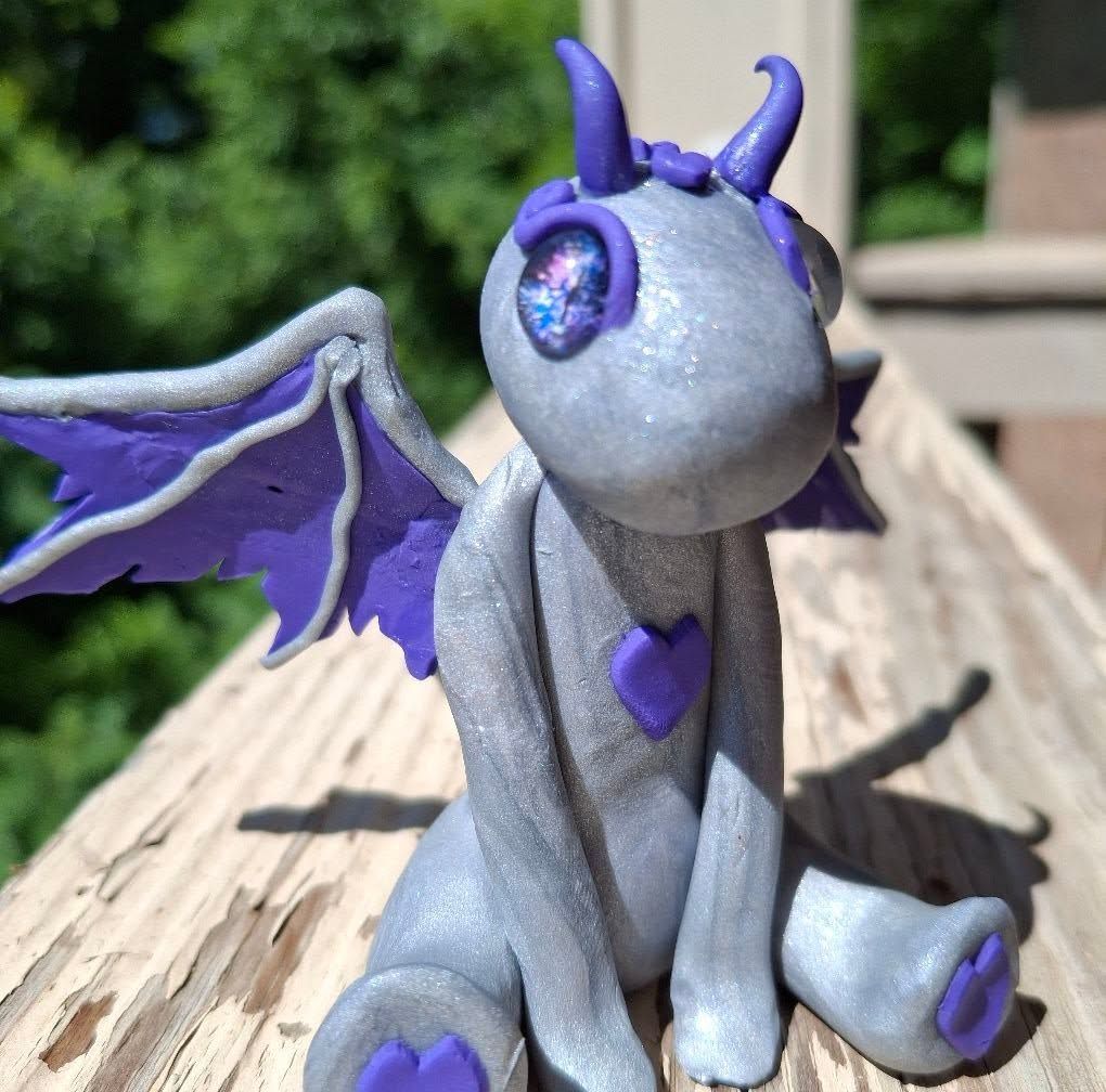 Purple-and-gray dragon figurine with wings sitting outdoors in sunlight